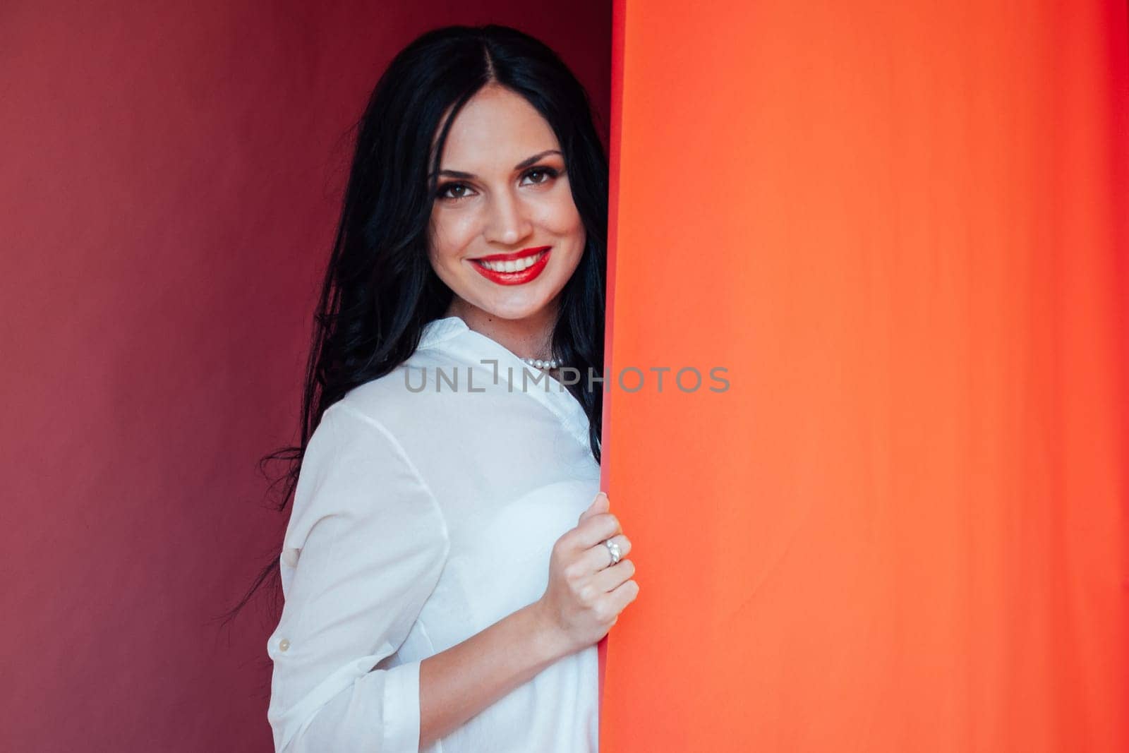 Portrait of happy satisfied beautiful brunette young woman with makeup in denim casual style standing and looking at camera with toothy smile. indoor studio shot, isolated on red background.
