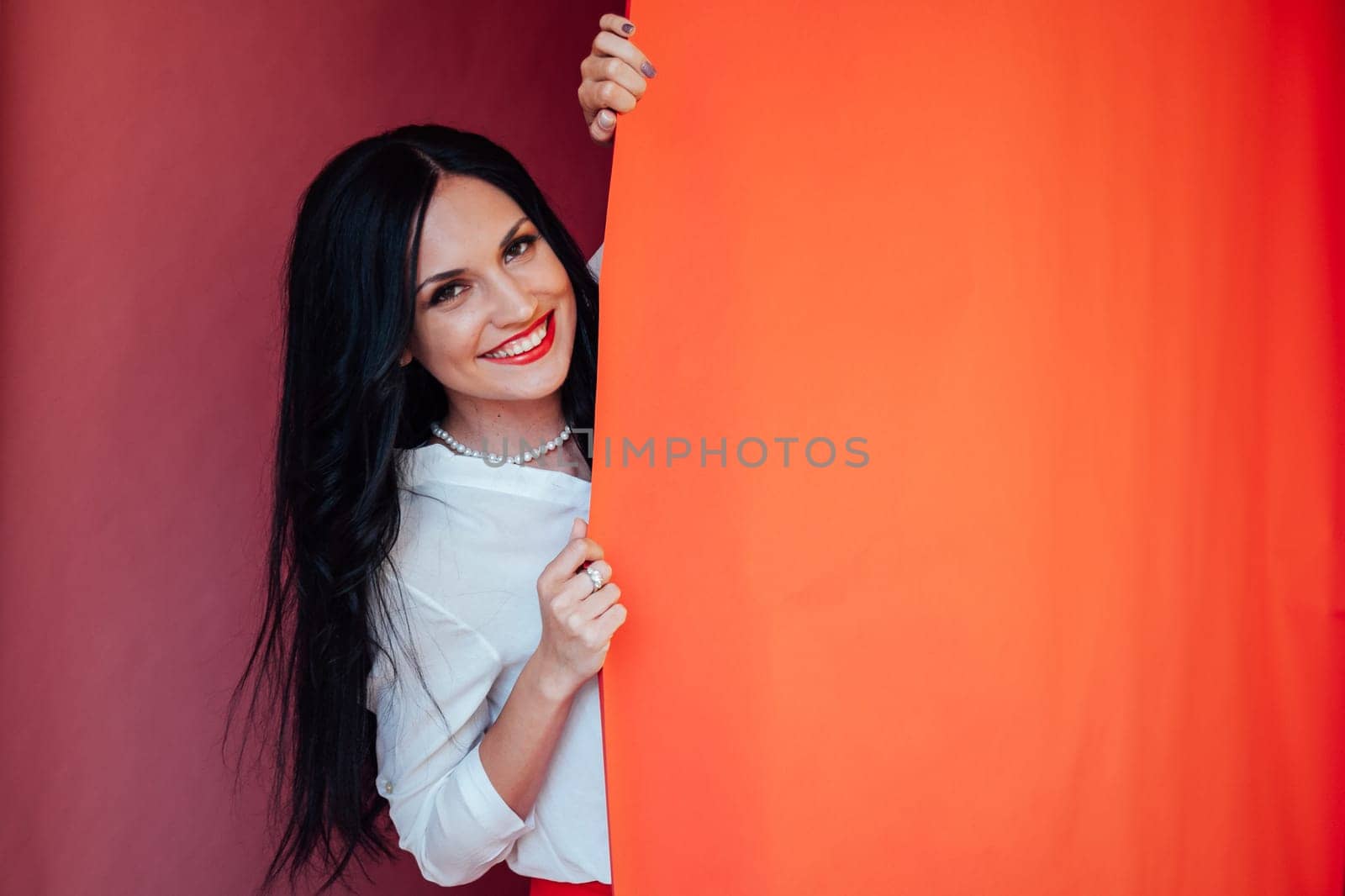 Portrait of happy satisfied beautiful brunette young woman with makeup in denim casual style standing and looking at camera with toothy smile. indoor studio shot, isolated on red background.