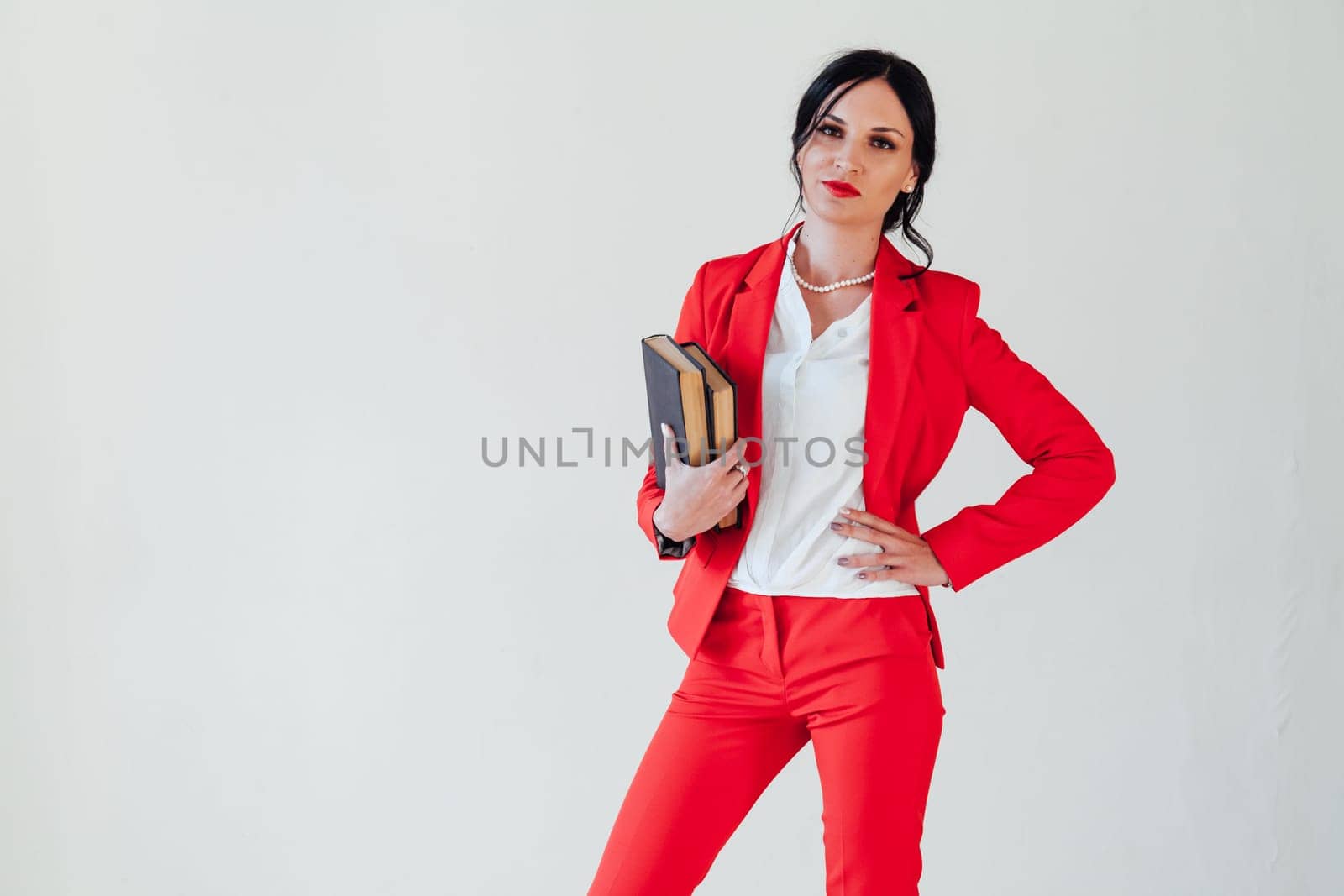 A young woman in a business suit, with a red book in hand, sitting on the wooden floor with a thoughtful face, glance to the side, full height.
