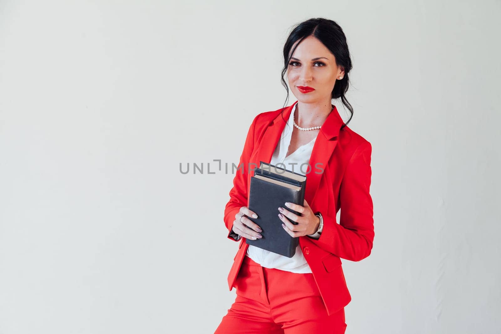 A young woman in a business suit, with a red book in hand, sitting on the wooden floor with a thoughtful face, glance to the side, full height.