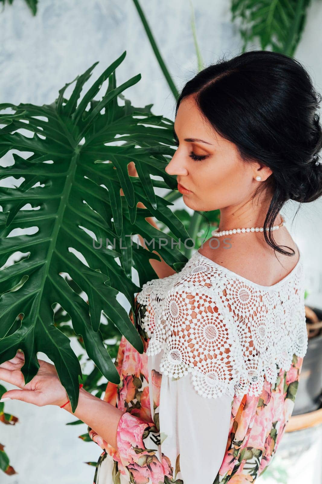 Beautiful brunette young woman relaxing and posing for camera on pink wall backgrorund. Lifestyle portrait of happy cheerful smiling adult caucasian female stands near palm tree with green branches