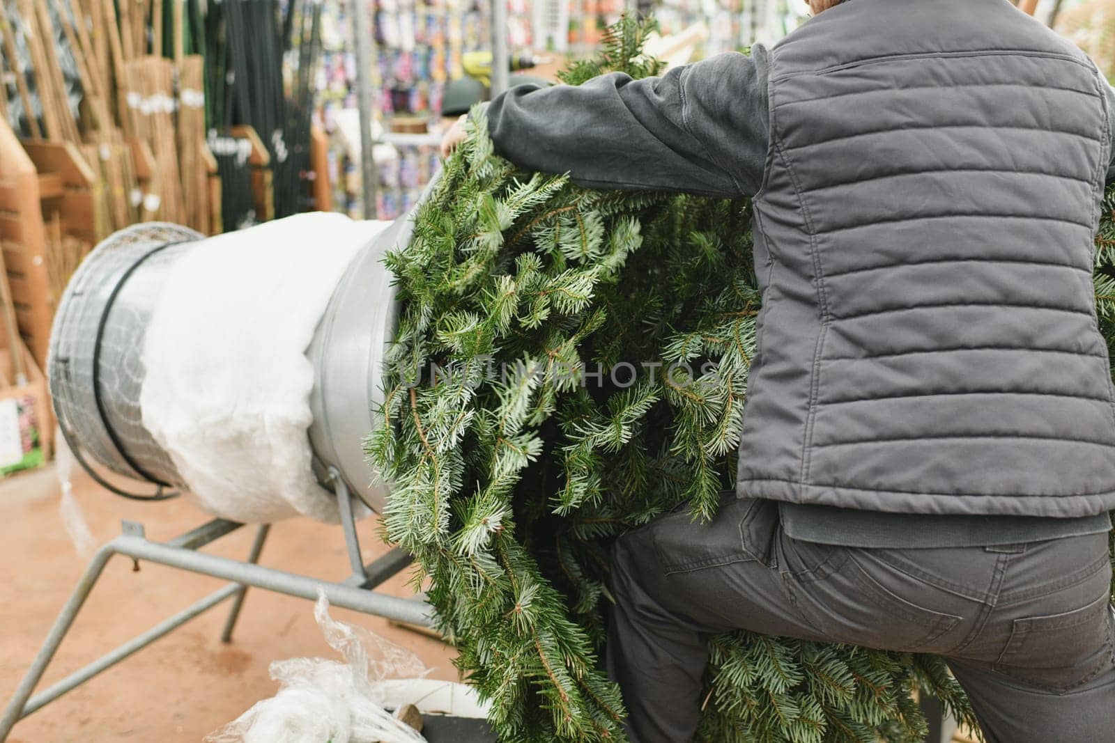 Salesman being wrapped up a Christmas tree packed in a plastic net by Godi