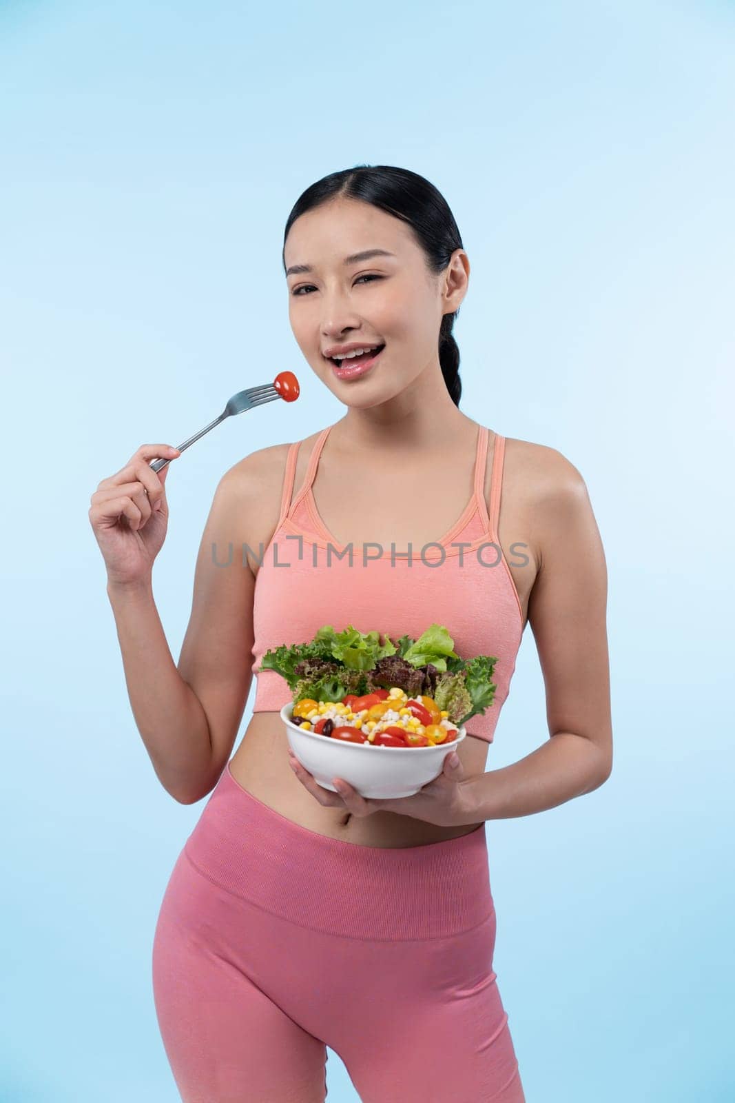 Young sporty Asian woman in sportswear holding salad bowl fill with vibrant of fruit and vegetable. Natural youthful and fit body lifestyle with balance nutrition on isolated background. Vigorous