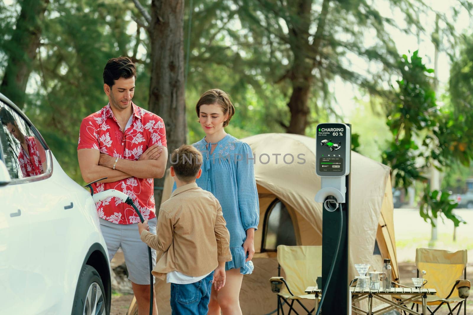 Outdoor adventure and family vacation camping in nature travel by eco friendly car for sustainable future. Lovely family recharge EV car with EV charging station in campsite. Perpetual