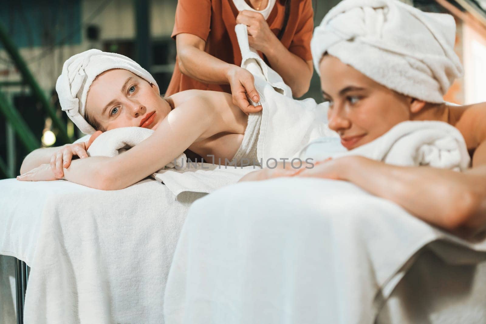 A portrait of a couple of a beautiful young caucasian woman with white towel rest on comfortable spa bed with relaxation while having body massage with professional masseur at spa salon.Tranquility.