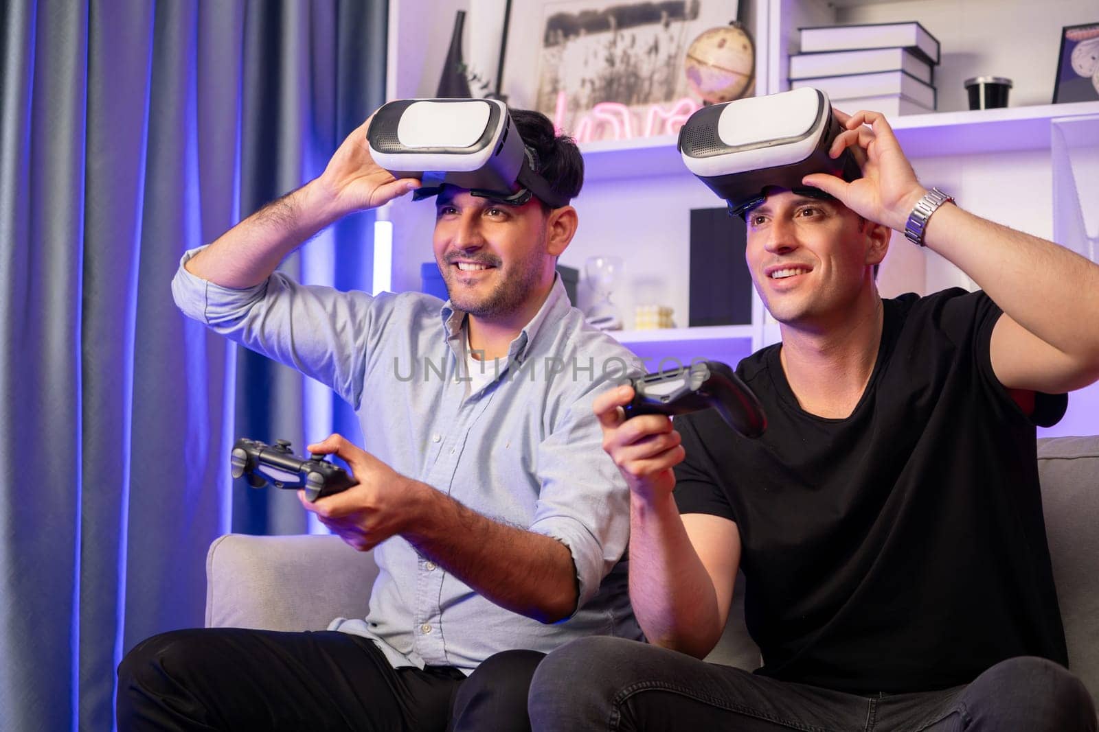 Buddy friend gamers playing video game using joysticks and VR headset of virtual technology in reality in studio room with neon blue light. Comfy living indoor with cheerful fighting winner. Sellable.