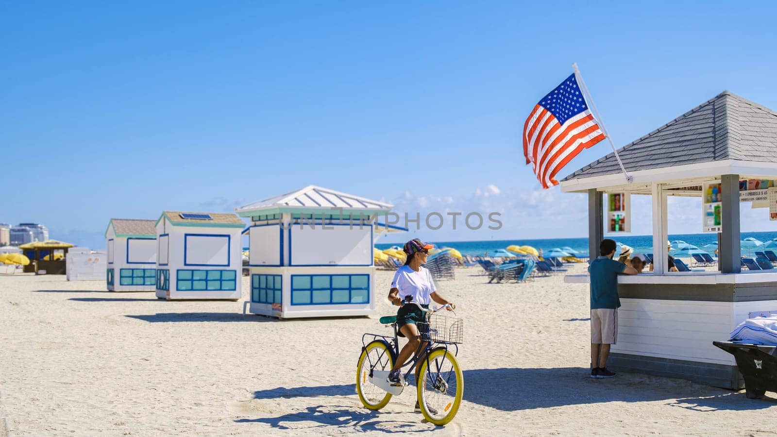 Young women on the beach in Miami with a bicycle, a colorful Miami beach, and a Lifeguard hut in South Beach, Florida. Asian women bicycle on the beach