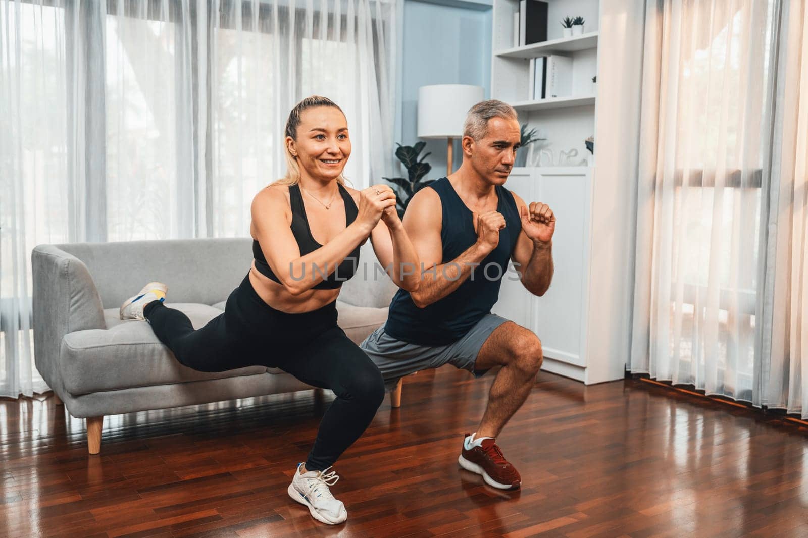 Active and fit senior couple warmup and stretching using furniture before home exercising routine at living room. Healthy fitness lifestyle concept after retirement for pensioner. Clout