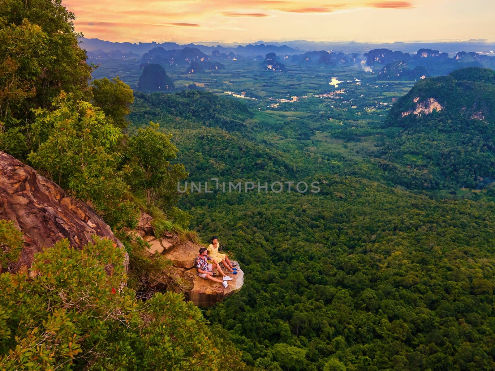 Dragon Crest Mountain Krabi Thailand, a Young couple of travelers sits on a rock that overhangs the abyss, Dragon Crest or Khuan Sai at Khao Ngon Nak Nature Trail in Krabi, Thailand