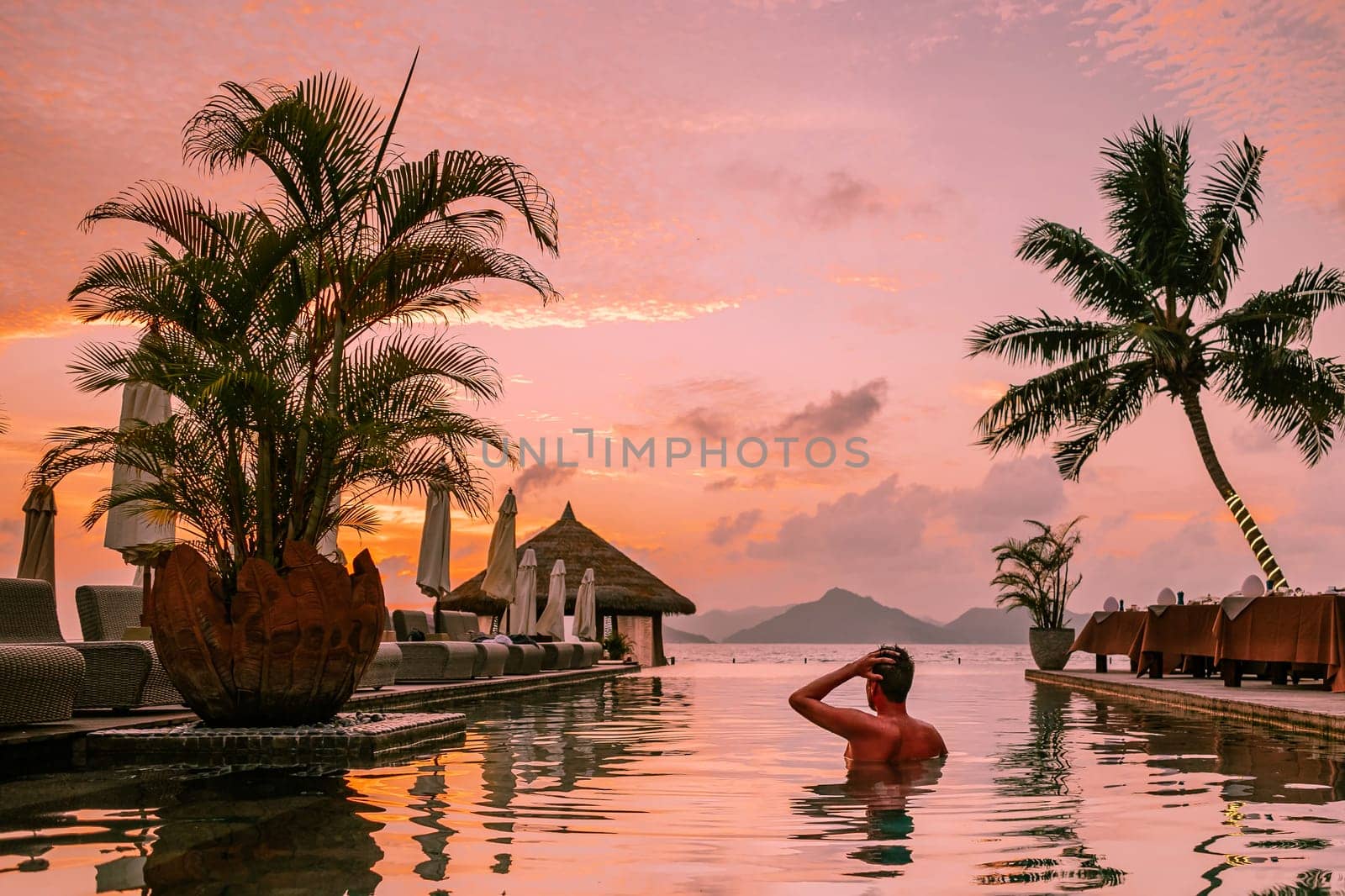 young men in a swimming pool during sunset, a Luxury swimming pool in a tropical resort, and relaxing holidays in the Seychelles islands. La Digue, a Young guy during sunset by the swimming pool