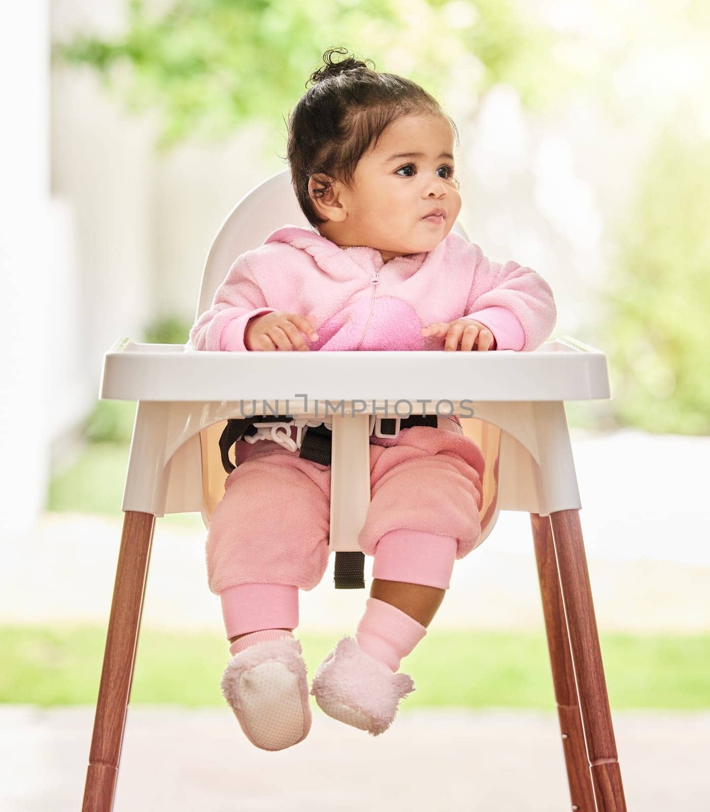 Baby, girl and sitting in feeding chair with thinking, curious and calm expression in home or apartment. Child, kid and relax with comfort, peace and security for development or hungry in house.