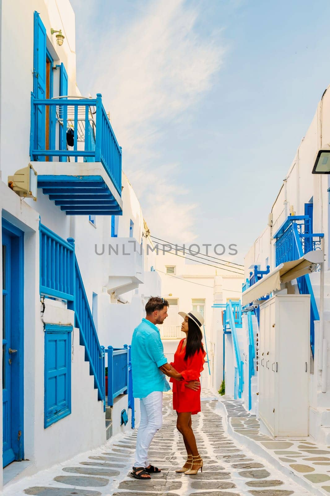 Romantic couple of men and women walking the street of Mykonos Greek village in Greece, colorful streets of Mikonos village in the morning