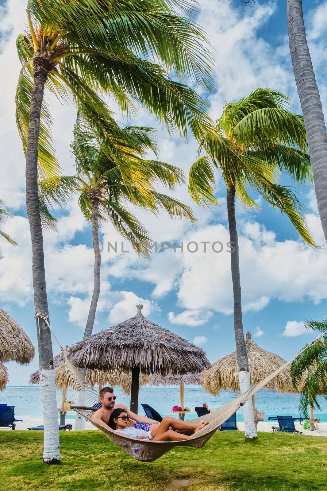 Palm Beach Aruba Caribbean, a couple of men and women in a hammock at a white long sandy beach with palm trees at Aruba Antilles during summer vacation holidays