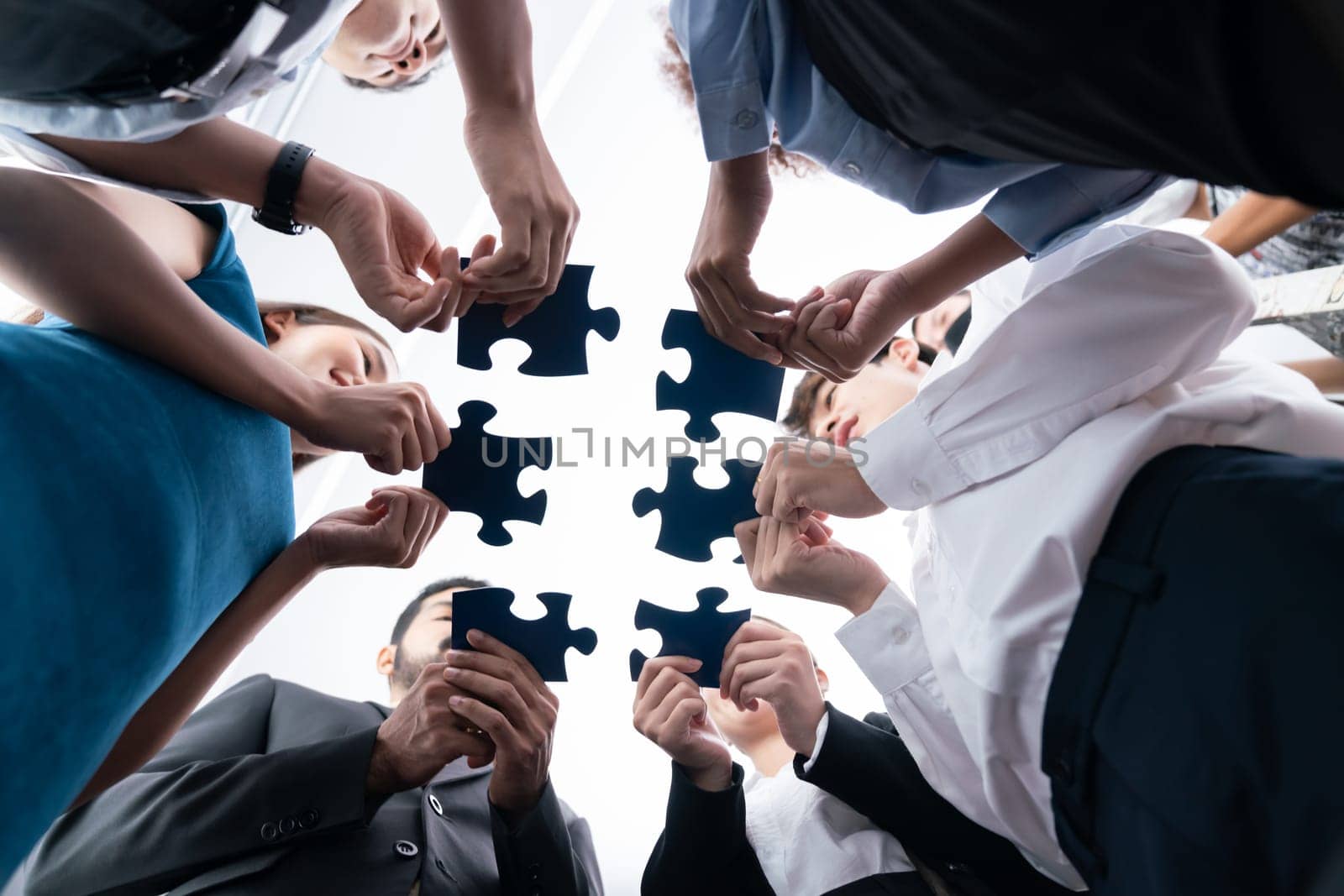 Below view of diverse corporate officer workers collaborate in office connecting puzzle pieces as partnership and teamwork concept. Unity and synergy in business idea by merging jigsaw puzzle. Concord