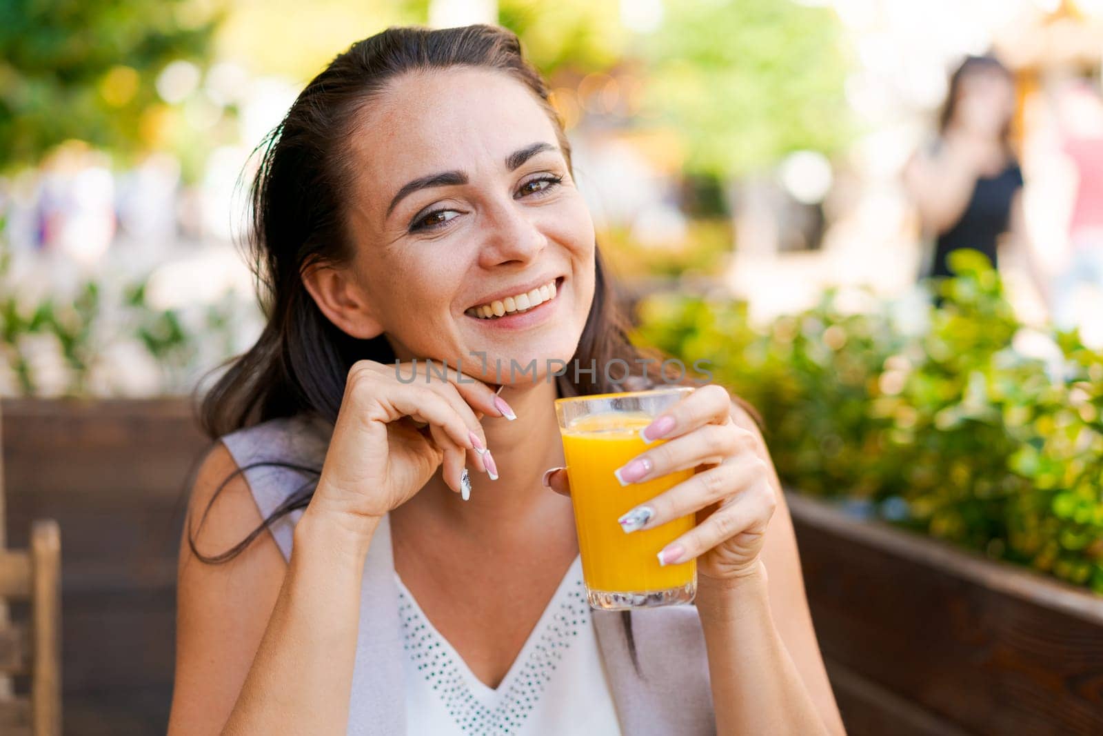 Happy business woman in street cafe drinks natural juice and smiles on sunny day