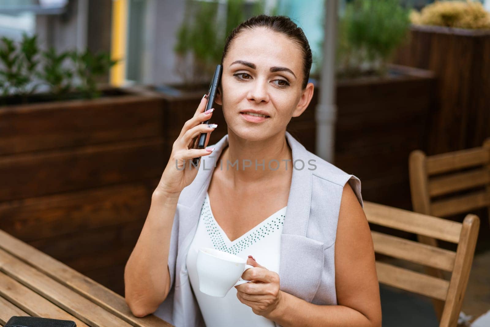 Business woman sitting in street cafe drinking coffee and talking on phone, coffee break concept