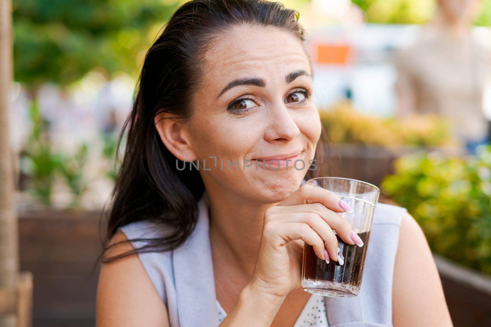 Happy business woman in street cafe drinks natural juice and smiles on sunny day