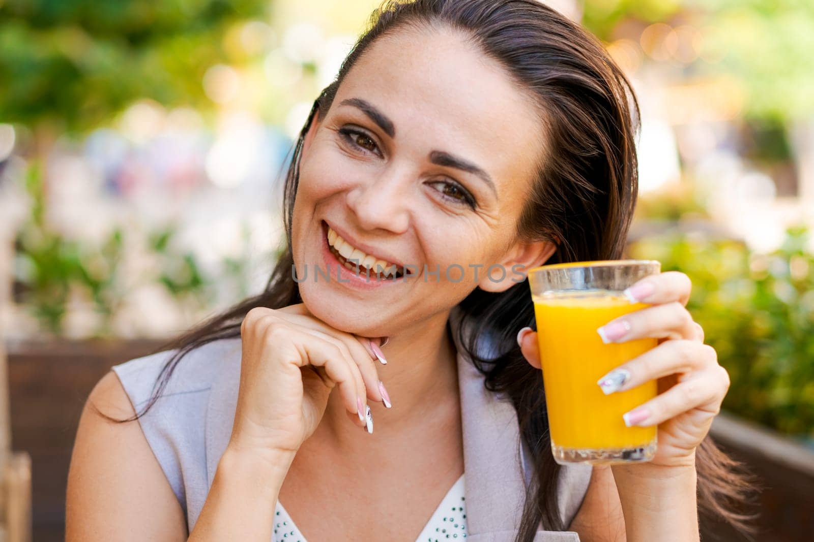 Happy business woman in street cafe drinks natural juice and smiles on sunny day