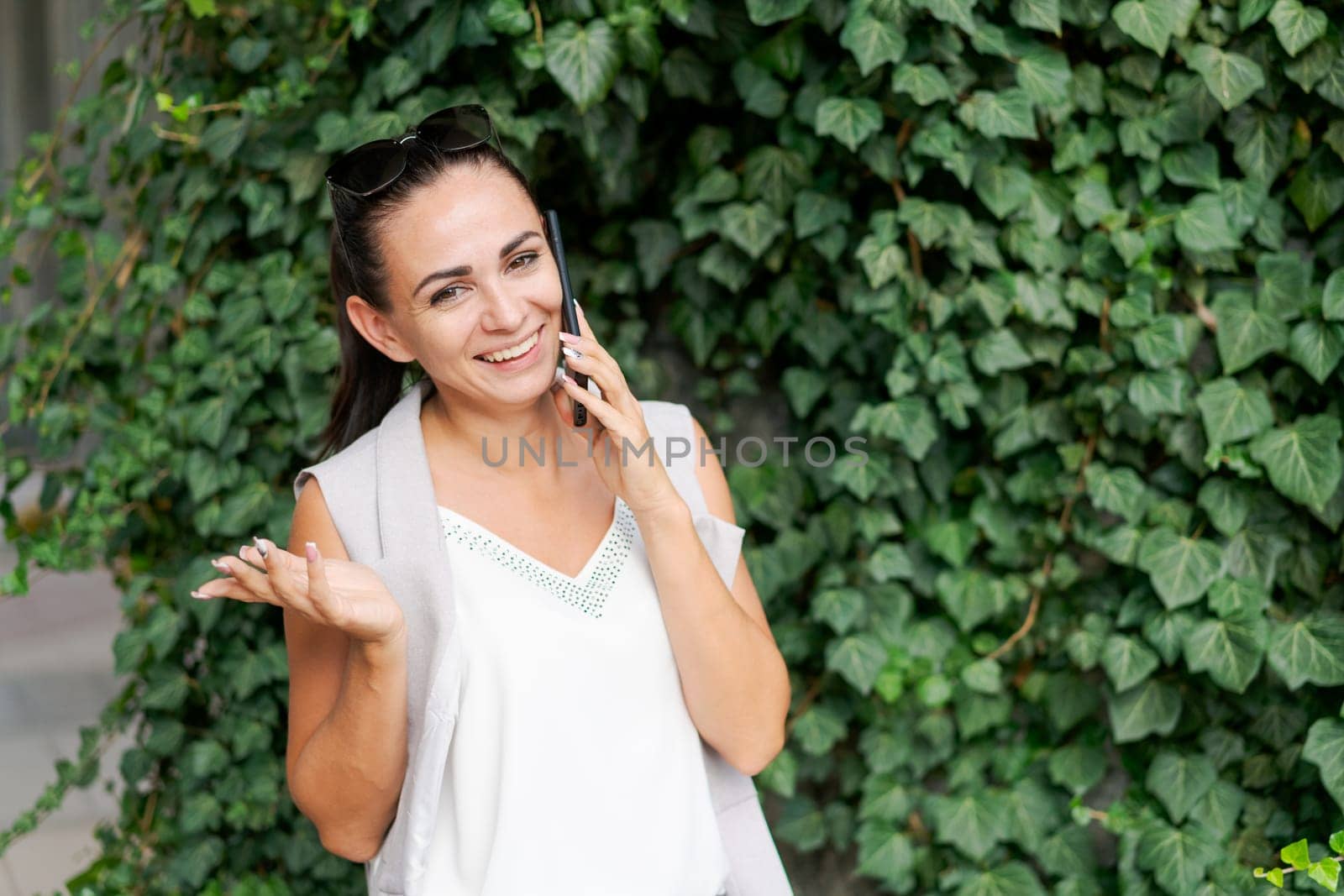 Attractive brunette businesswoman talking on mobile phone. Caucasian business woman smiling during a telephone conversation. Against a background of greenery