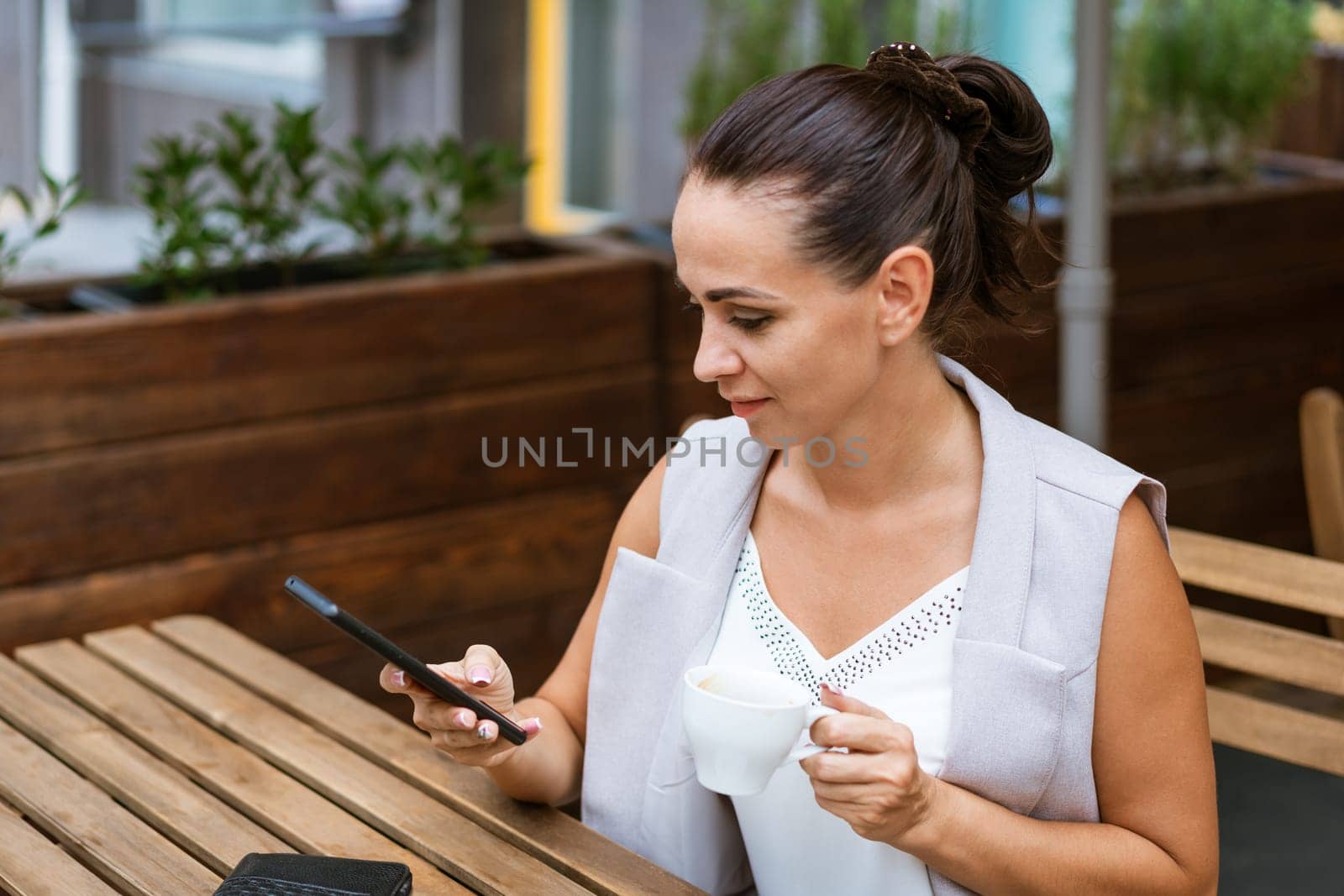 Business woman sitting in street cafe drinking coffee and talking on phone by EkaterinaPereslavtseva