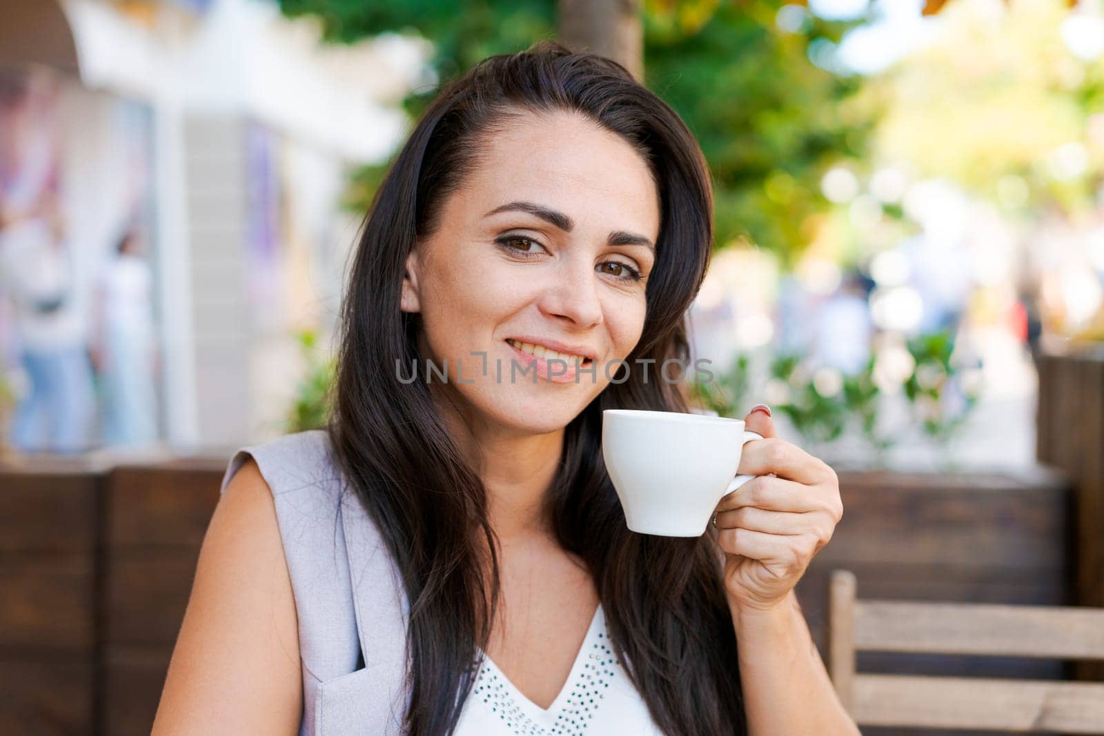 Happy smiling business brunette drinking coffee in a street cafe. Coffee break, lifestyle concept. Outdoor portrait