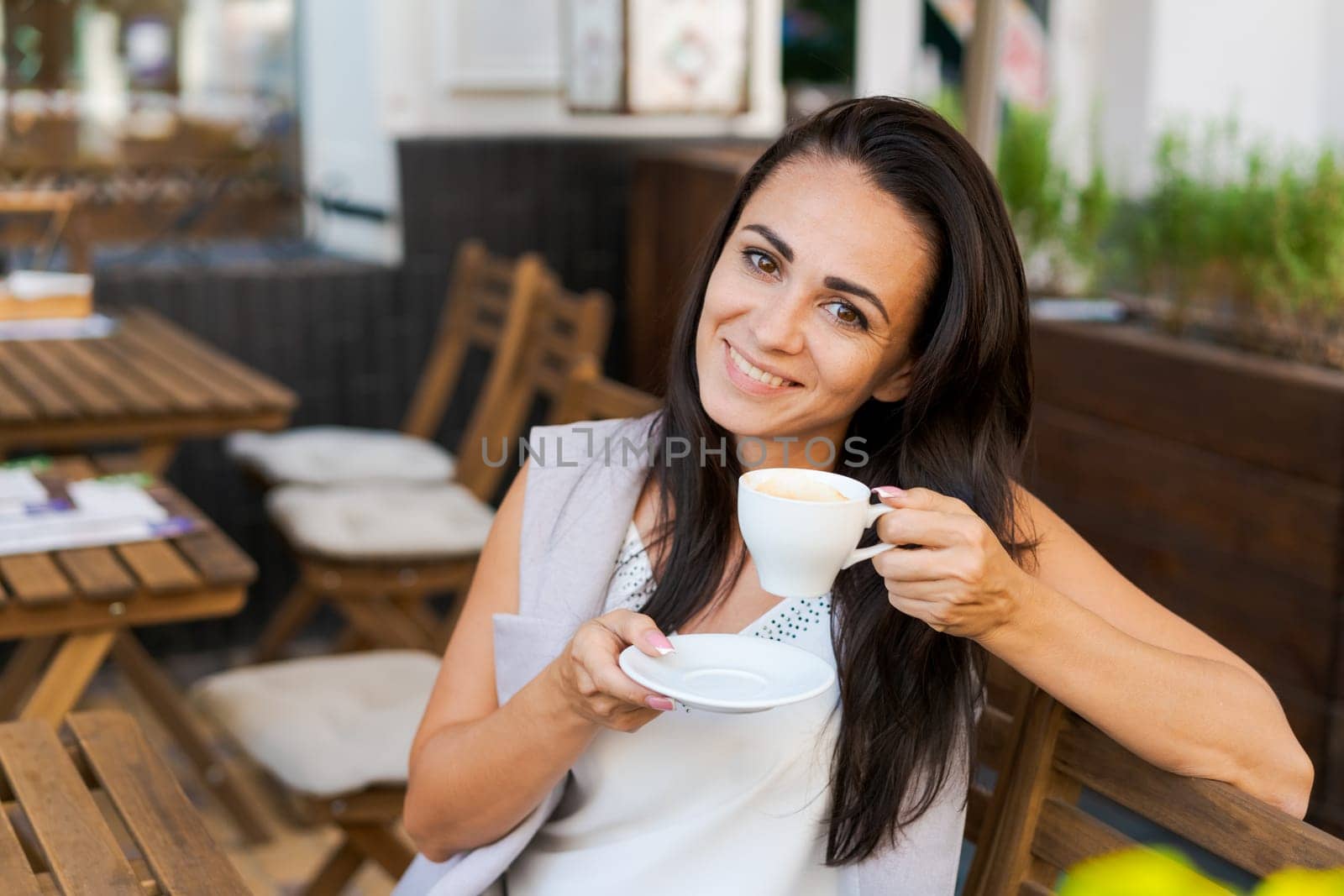 Positive business woman sitting in outdoor cafe drinking coffee