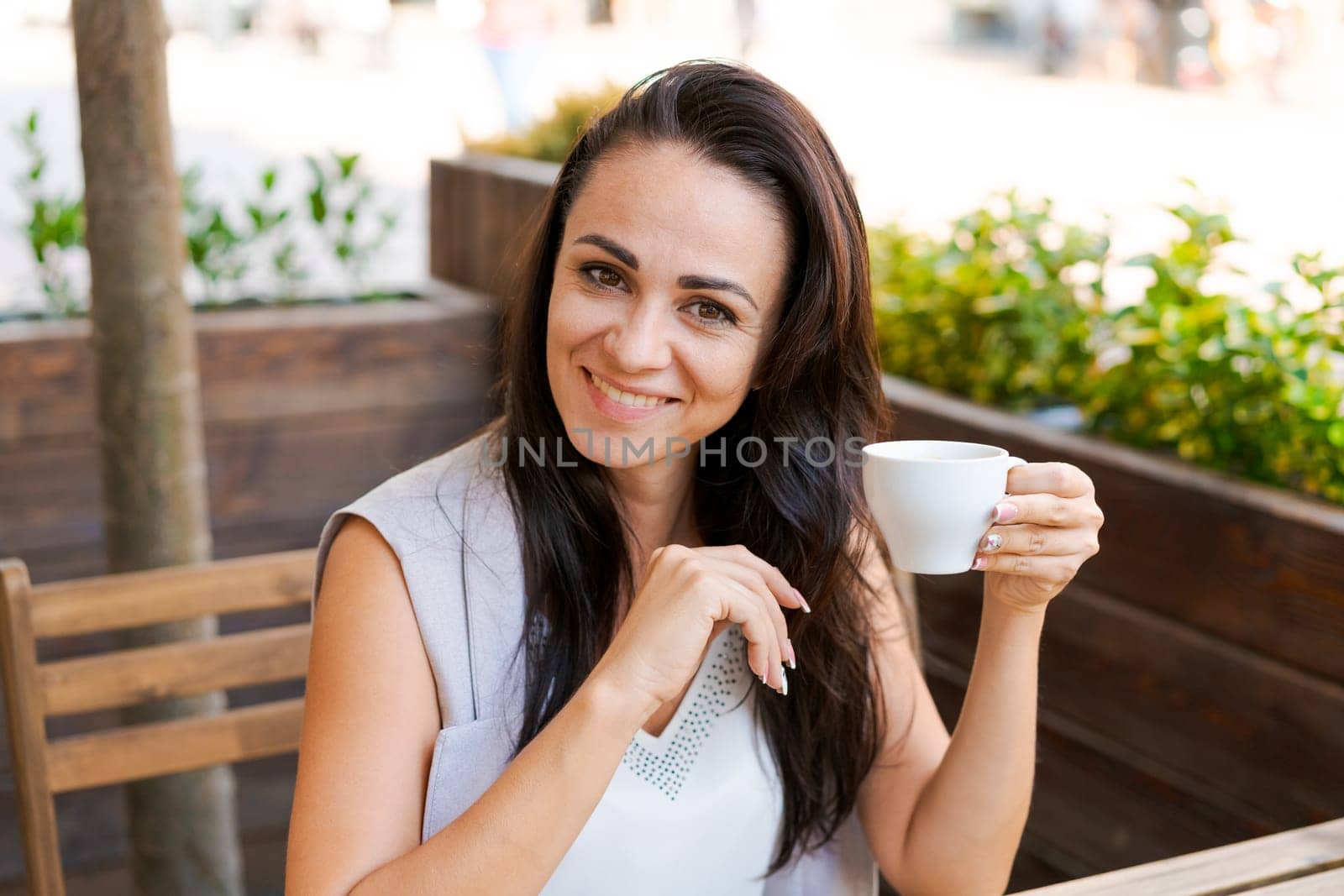 Positive business woman sitting in outdoor cafe drinking coffee