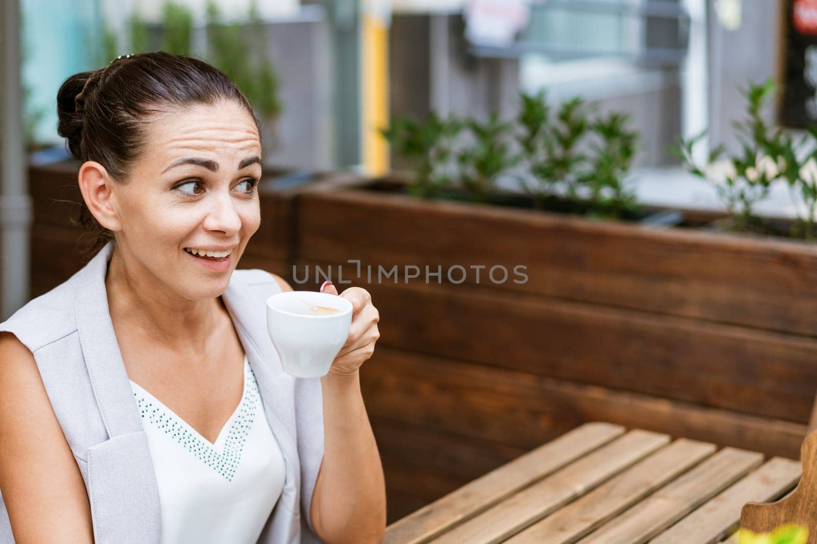 Positive business woman sitting in outdoor cafe drinking coffee. by EkaterinaPereslavtseva