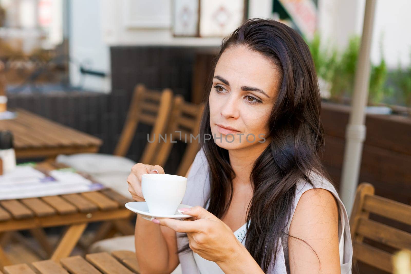 Positive business woman sitting in outdoor cafe drinking coffee. by EkaterinaPereslavtseva