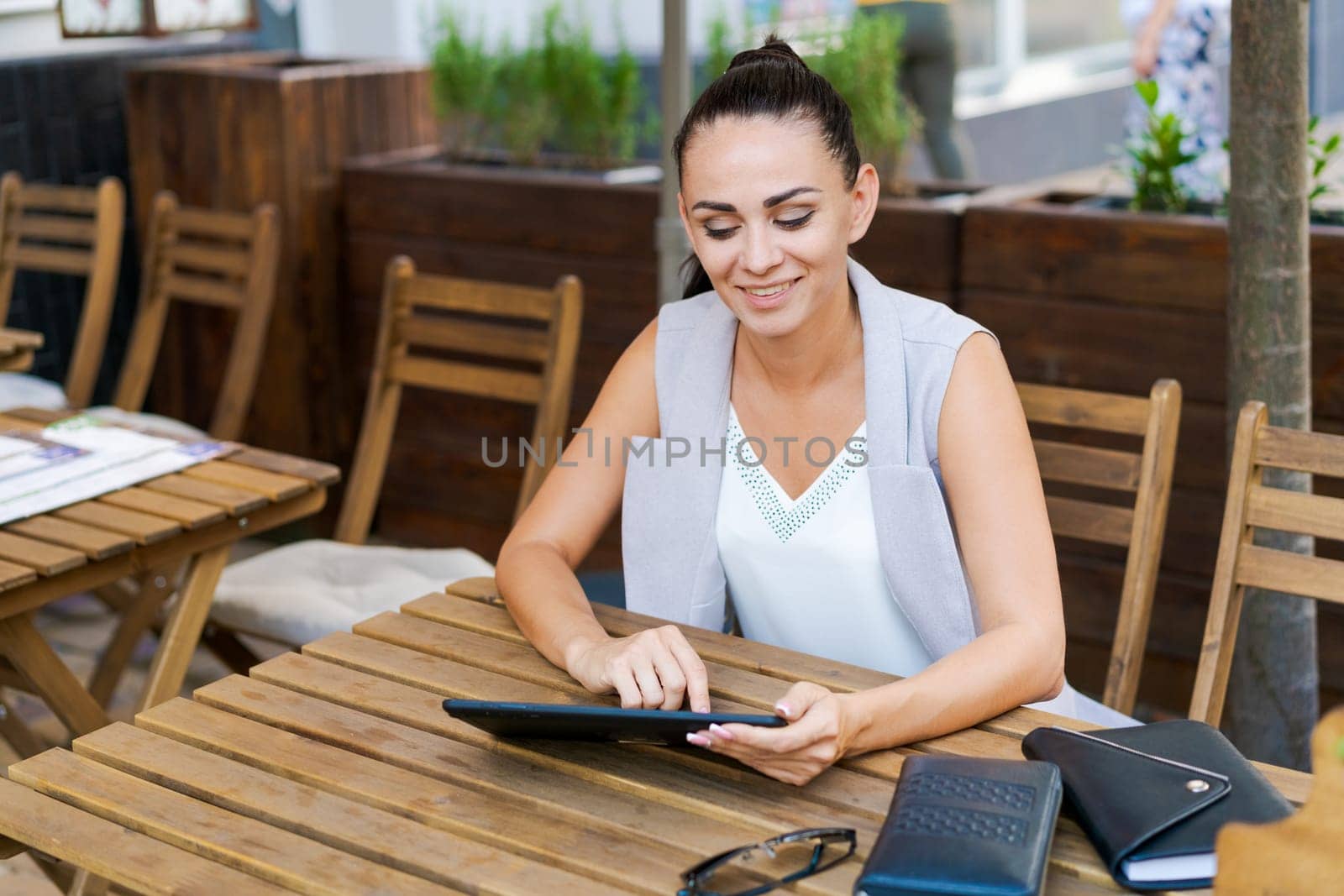 Beautiful businesswoman with smile sitting with touchpad in cozy restaurant while relaxing outside, happy female student working on a digital tablet and relaxing in a cafe after university