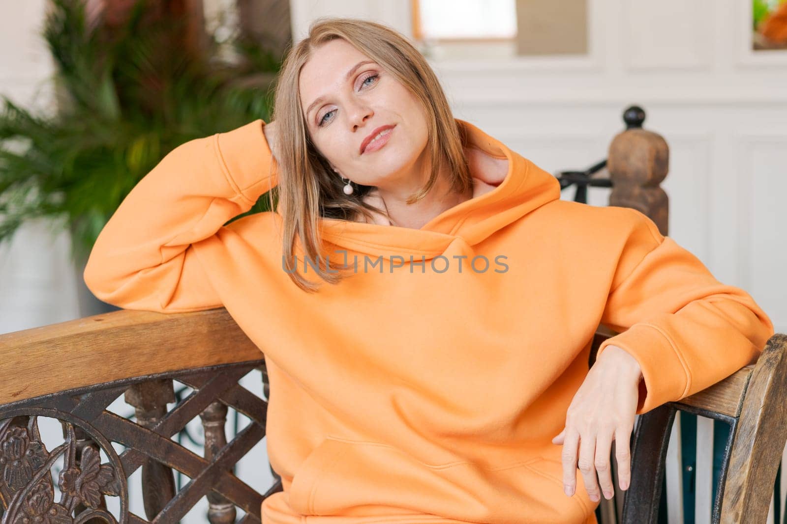 Cute woman in cafe. Portrait beautiful woman, alone at table in cafe. Concept waiting for an order. In a bright orange sweatshirt