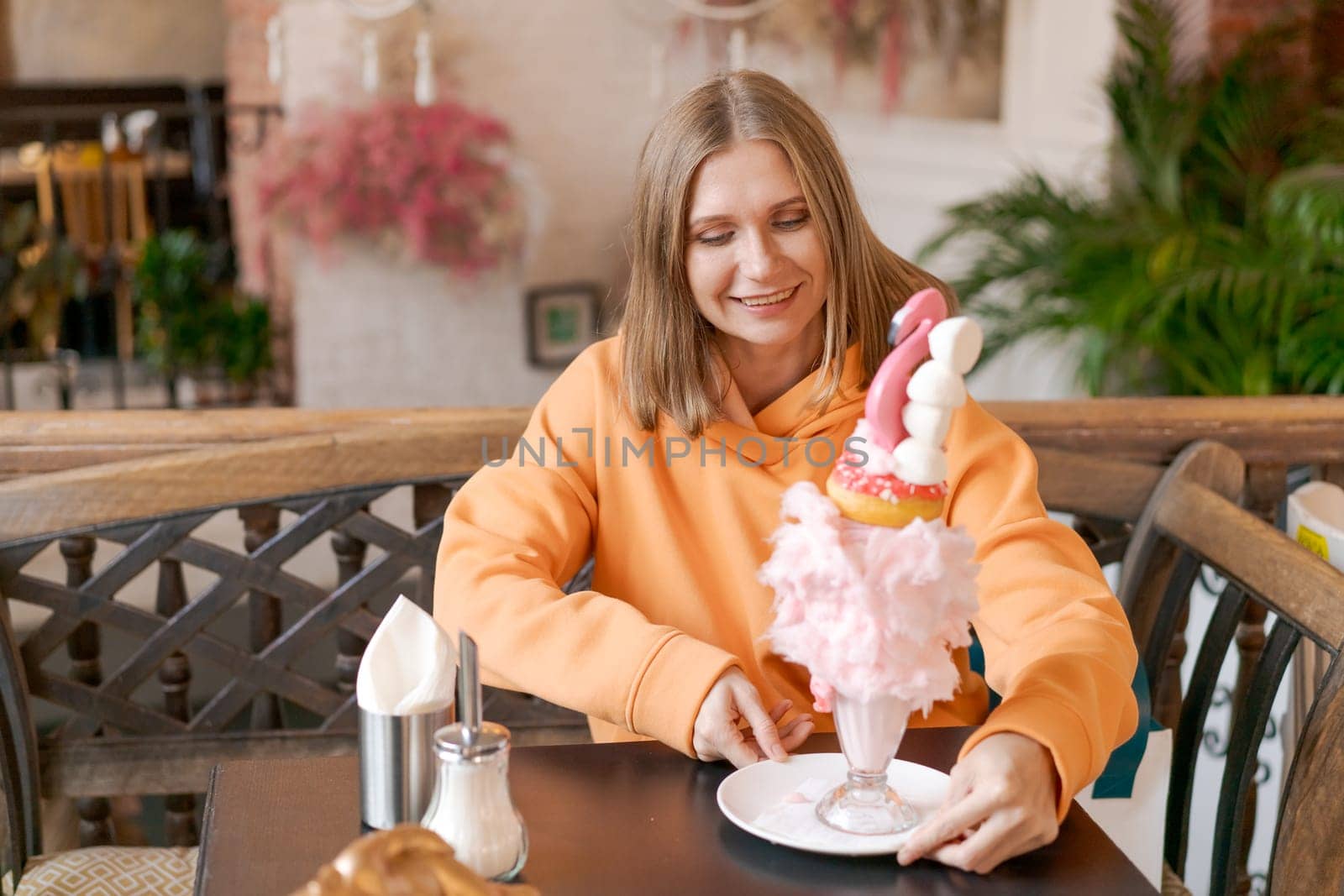 Happy woman eating sweet dessert in form pink flamingo in restaurant, woman sitting in a cafe and enjoying a sweet dessert for lunch, sweet tooth concept