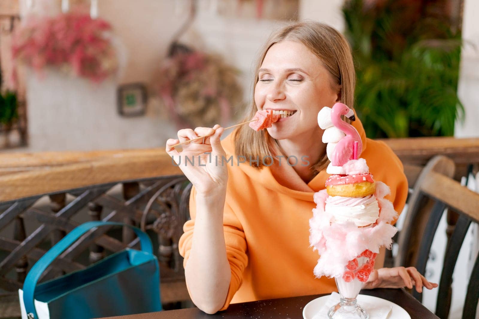 Beautiful woman eats dessert in form pink flamingo in cafe. Time for fun, vows in a bright sweatshirt