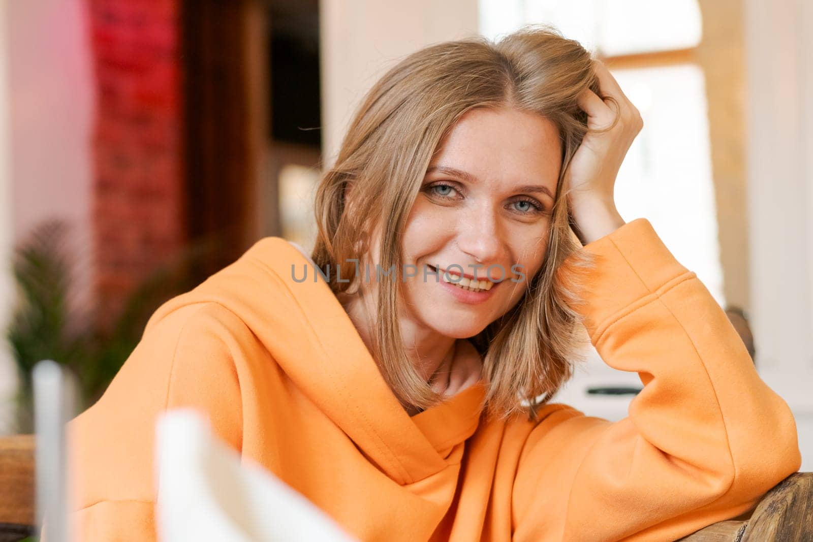 Portrait happy woman in cafe. Wearing a bright orange sweatshirt. by EkaterinaPereslavtseva