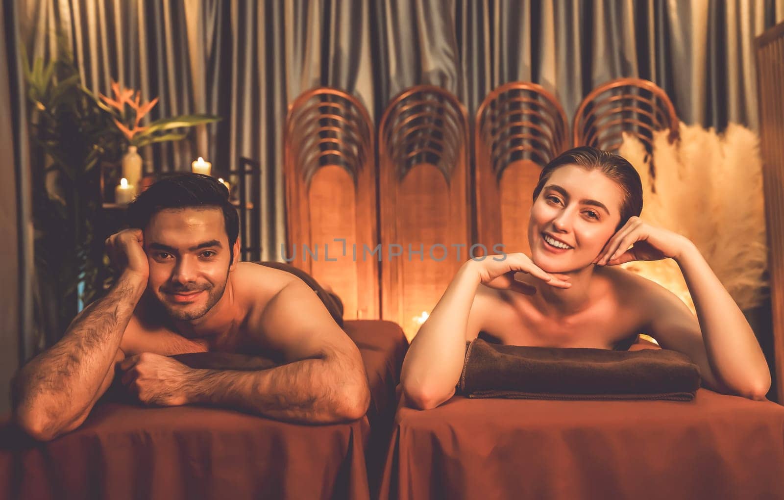 Caucasian couple customer enjoying relaxing anti-stress spa massage and pampering with beauty skin recreation leisure in warm candle lighting ambient salon spa at luxury resort or hotel. Quiescent