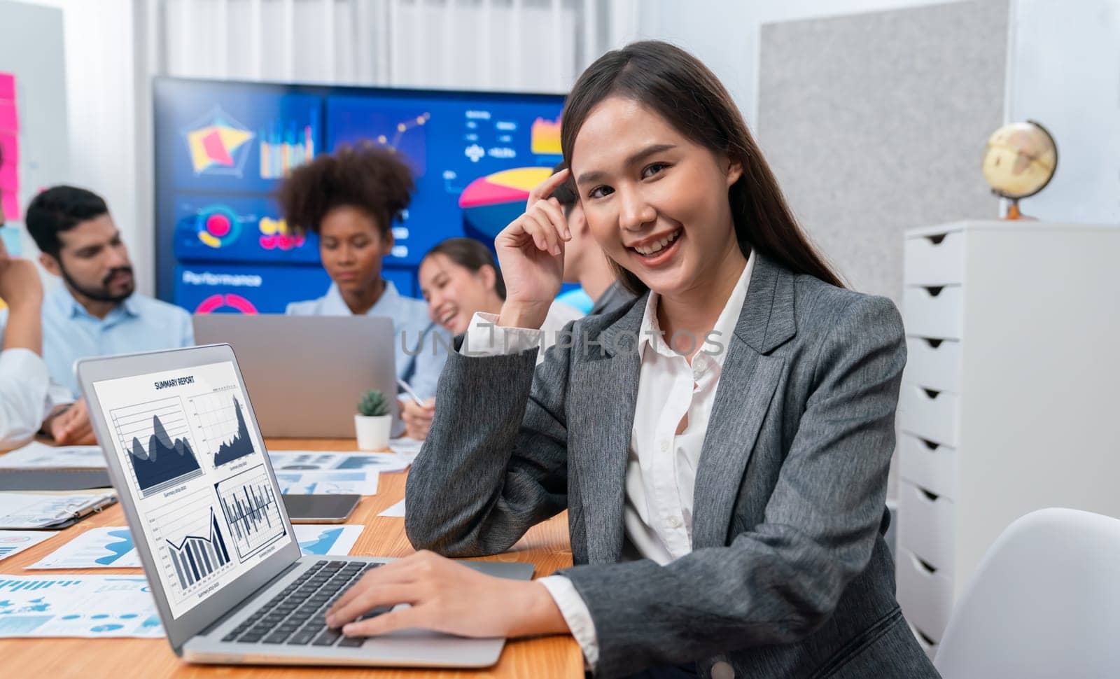 Portrait of happy young asian businesswoman with group of office worker on meeting with screen display business dashboard in background. Confident office lady at team meeting. Concord