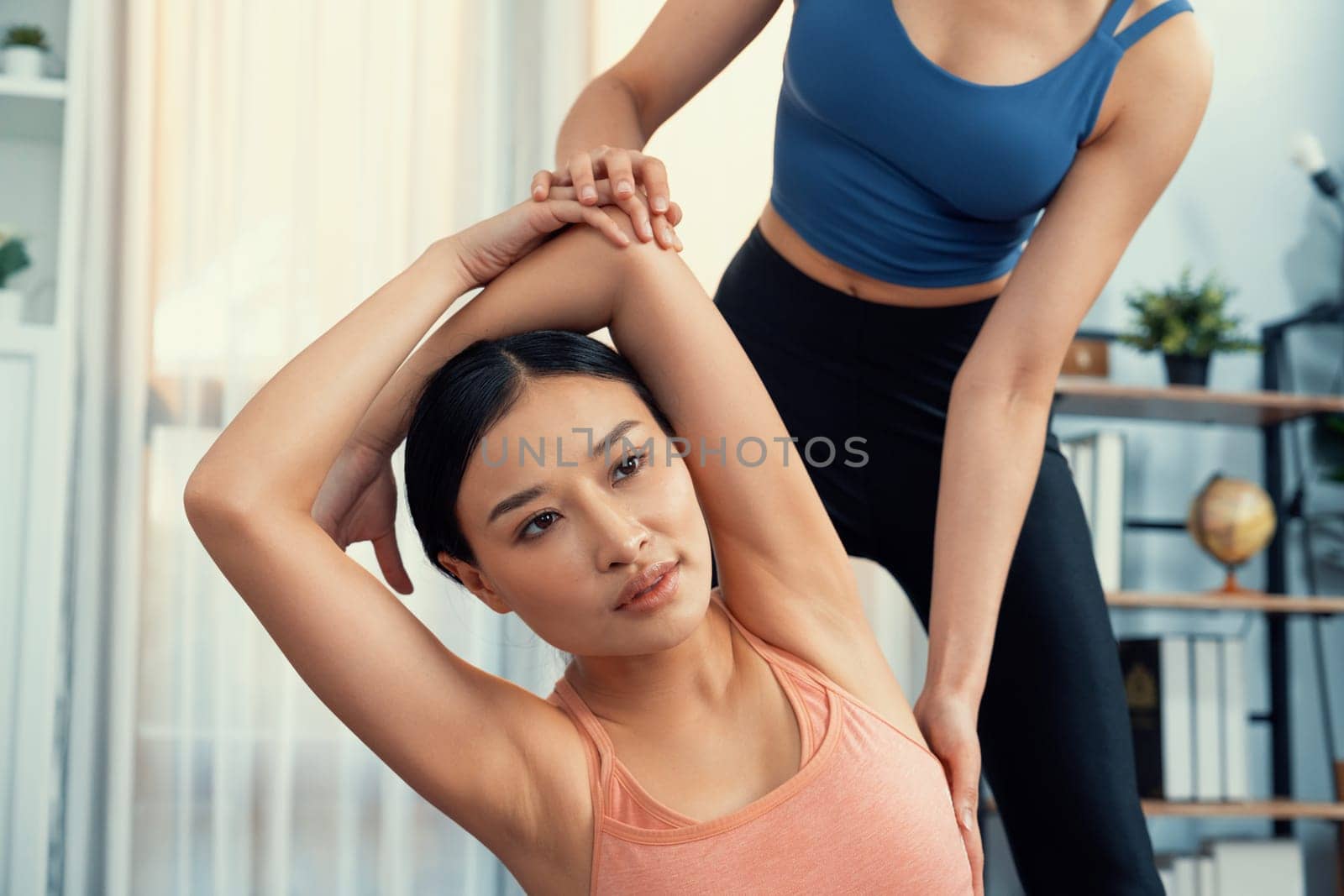 Asian woman in sportswear doing yoga exercise on fitness mat with trainer or workout buddy as home workout training routine. Healthy body care in yoga lifestyle people. Vigorous