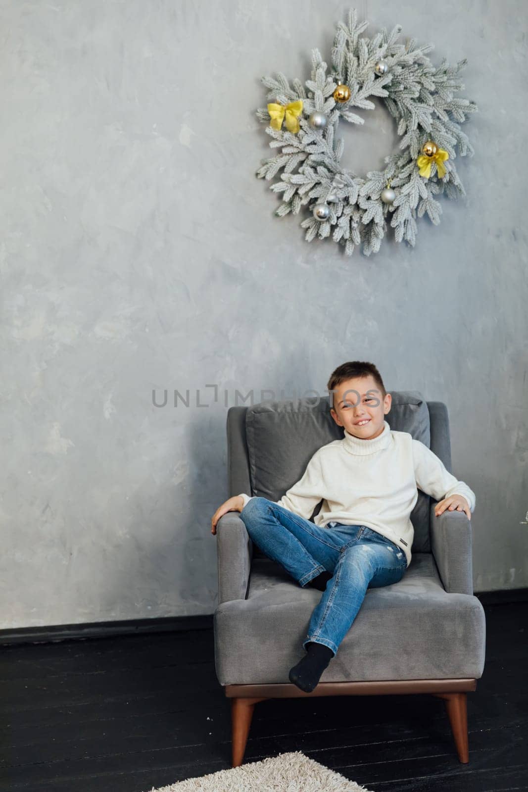 Boy sitting in armchair at christmas wreath for new year by Simakov