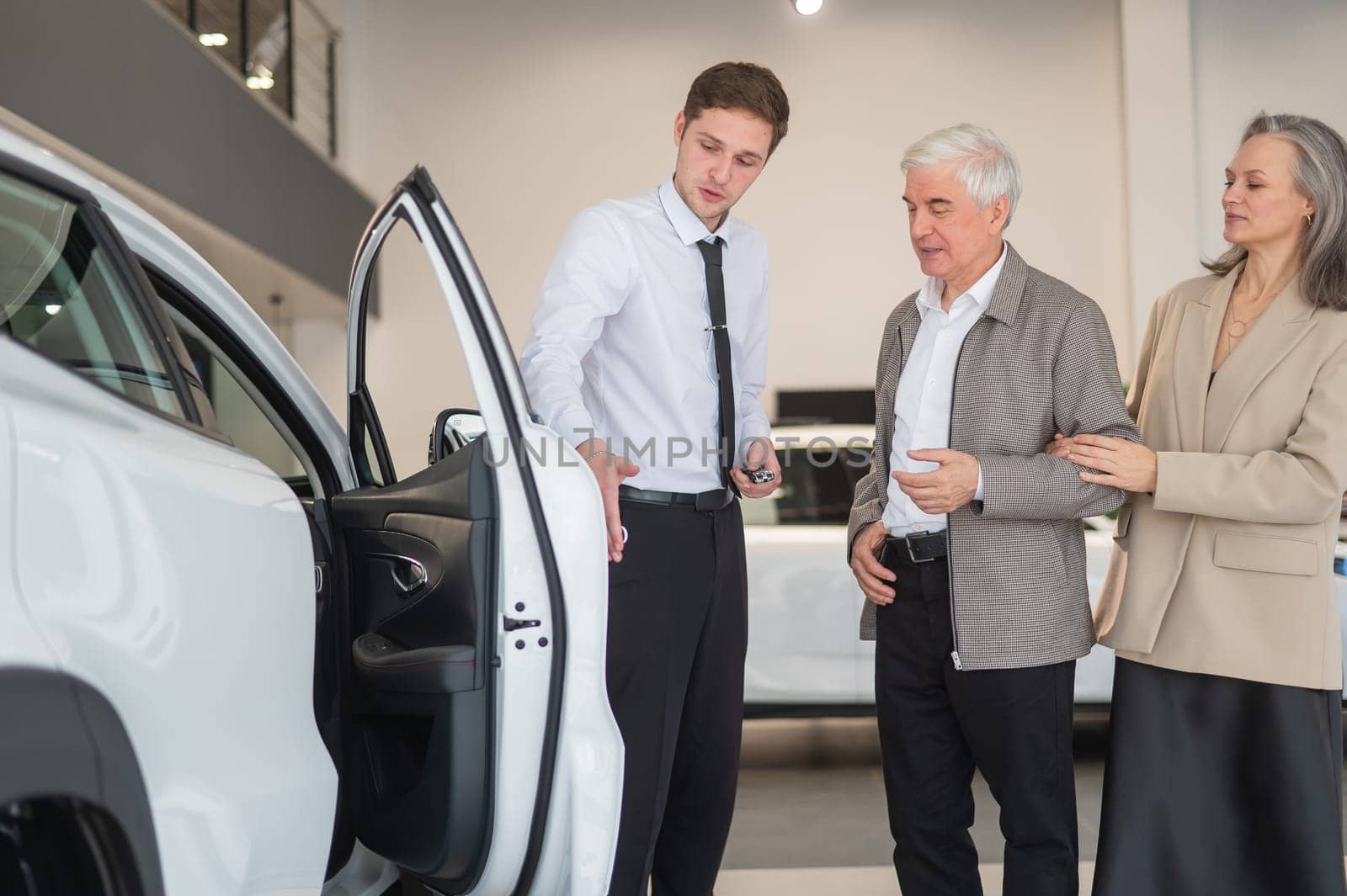 A salesman in a car dealership shows a car to a mature married couple. by mrwed54