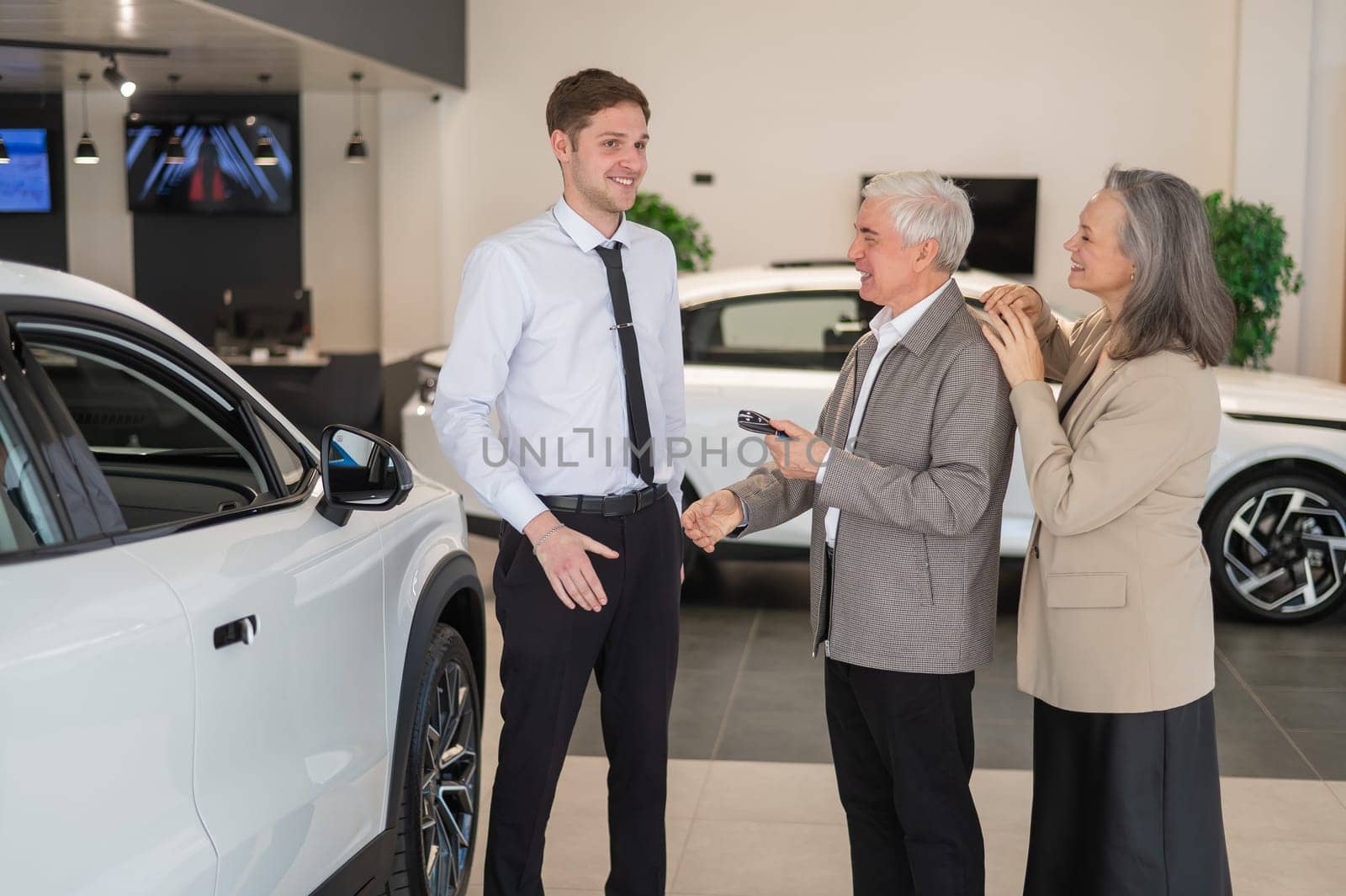 A salesman hands over the keys to a new car to an elderly Caucasian couple