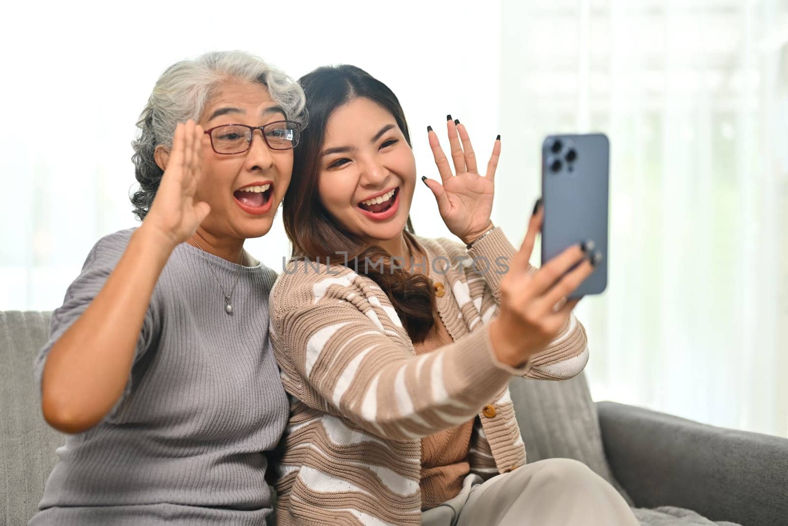 Overjoyed adult daughter and senior mother taking selfie with smartphone at home.