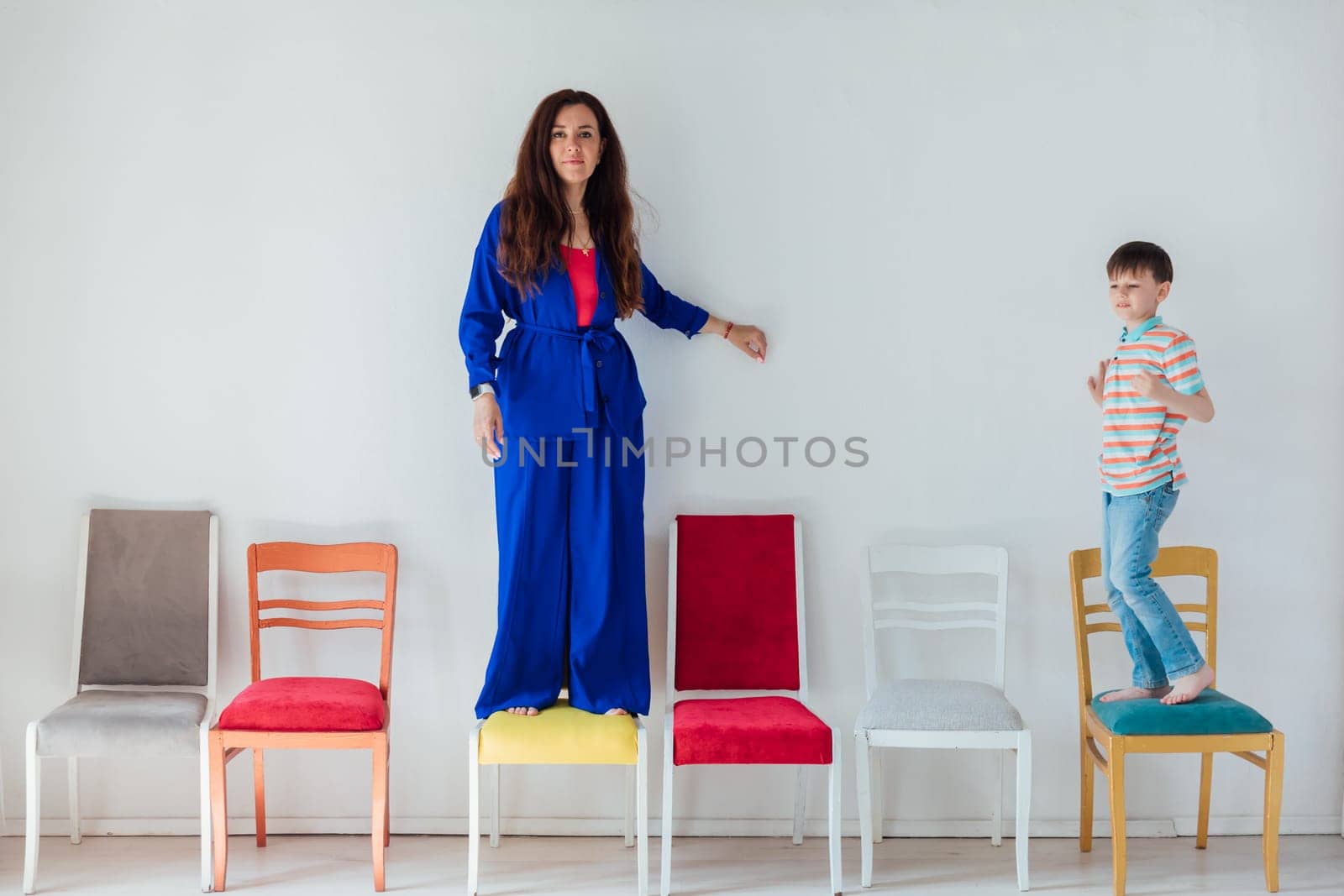 Boy and woman and many different chairs in the interior of a white room