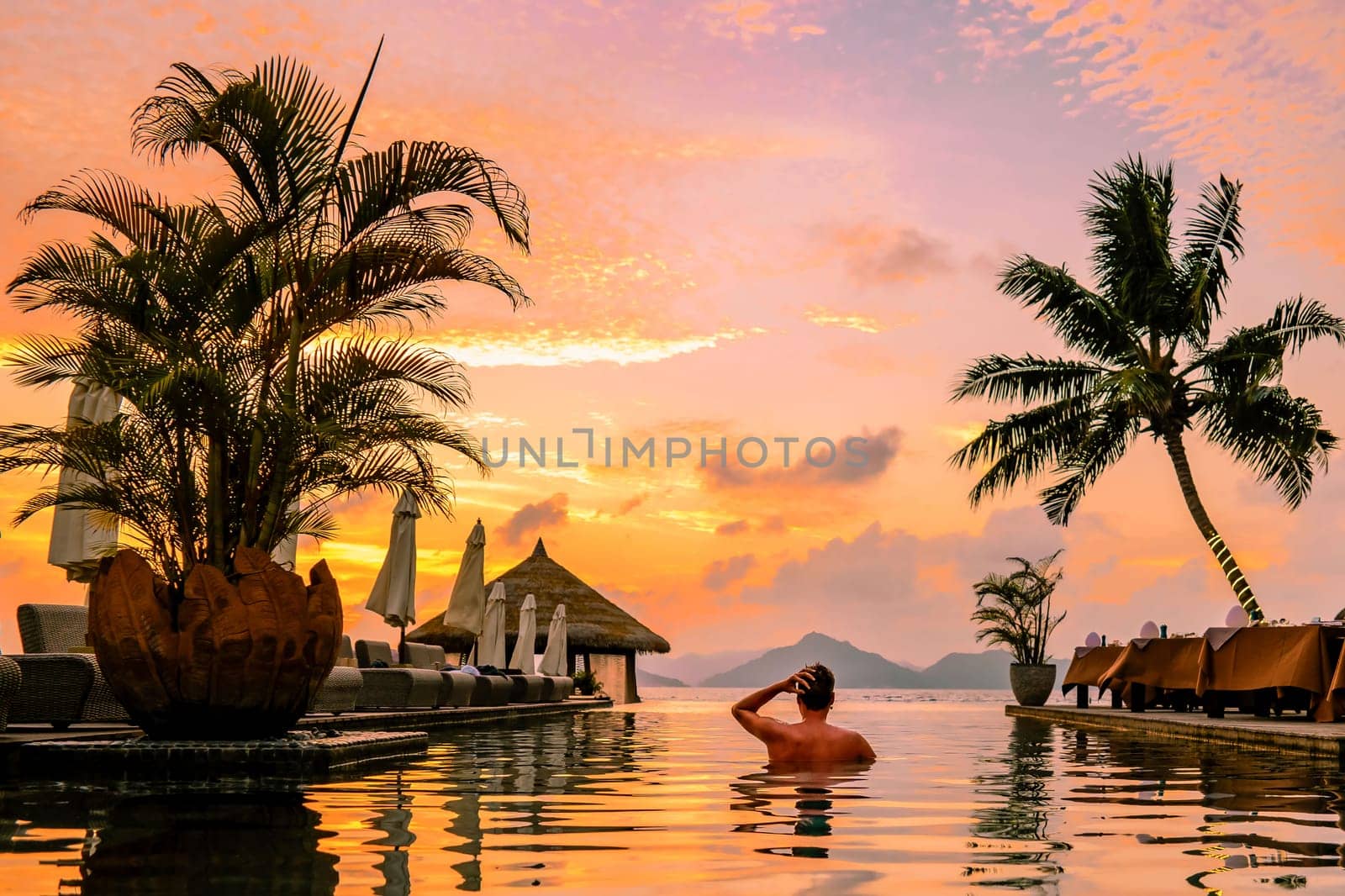 young men in swimming pool during sunset, Luxury swimming pool in tropical resor by fokkebok