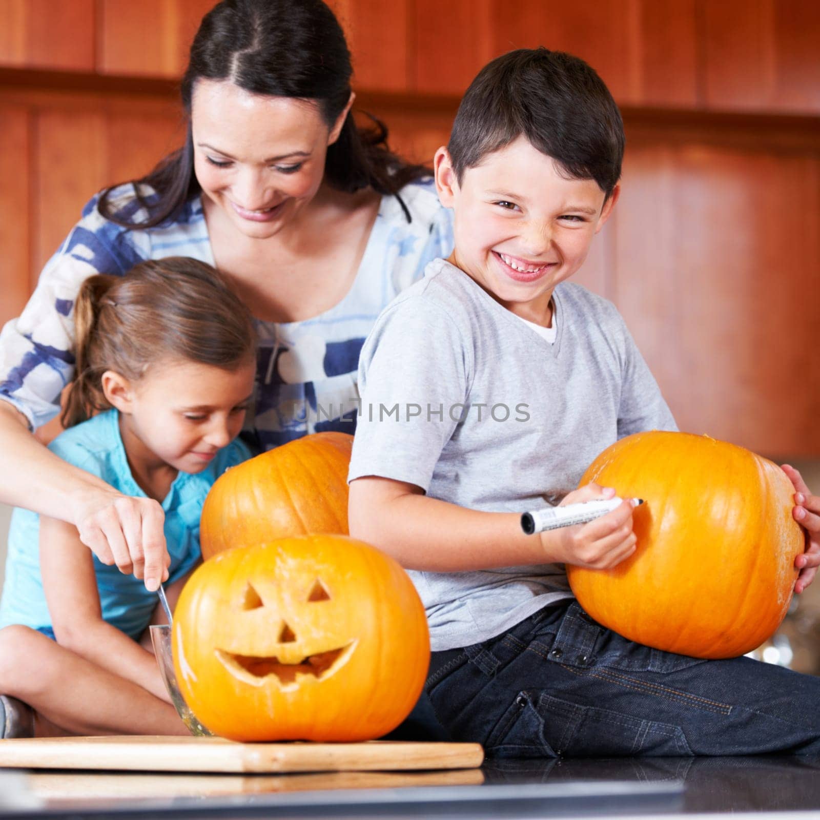 Halloween, pumpkin and a family in the kitchen of their home together for holiday celebration. Creative, smile or happy with a mother, son and daughter carving a face into a vegetable for decoration.