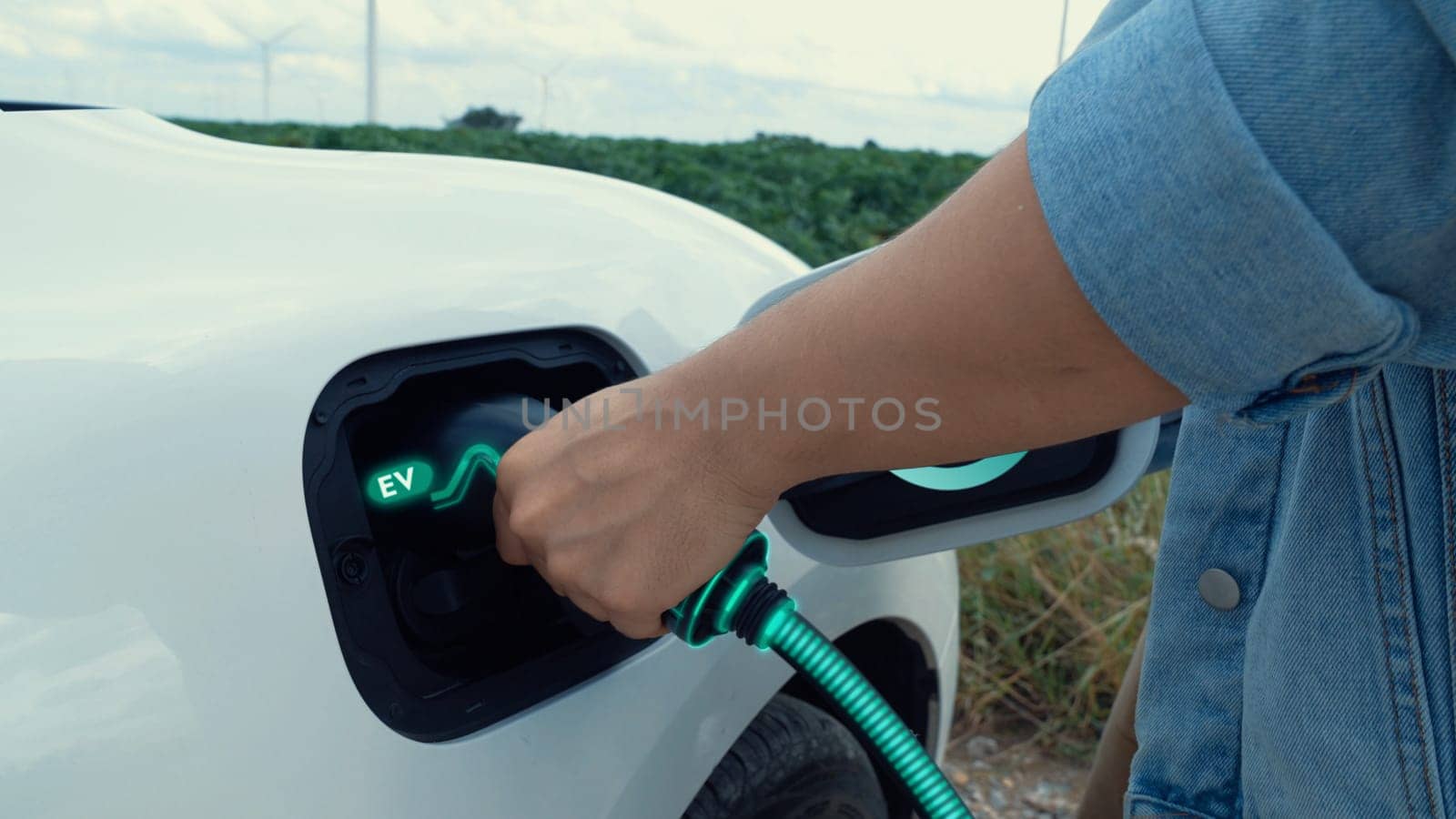 Hand insert EV charger and recharge electric car from charging station on nature and travel concept background. Technological advancement of alternative energy sustainability and EV car. Peruse