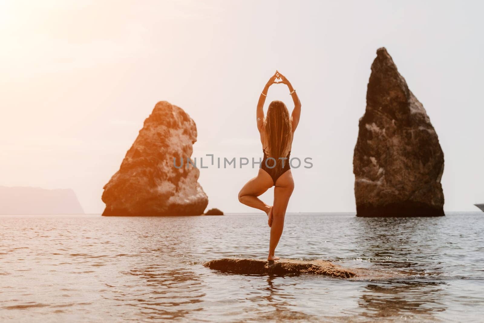 Woman sea yoga. Back view of free calm happy satisfied woman with long hair standing on top rock with yoga position against of sky by the sea. Healthy lifestyle outdoors in nature, fitness concept. by panophotograph