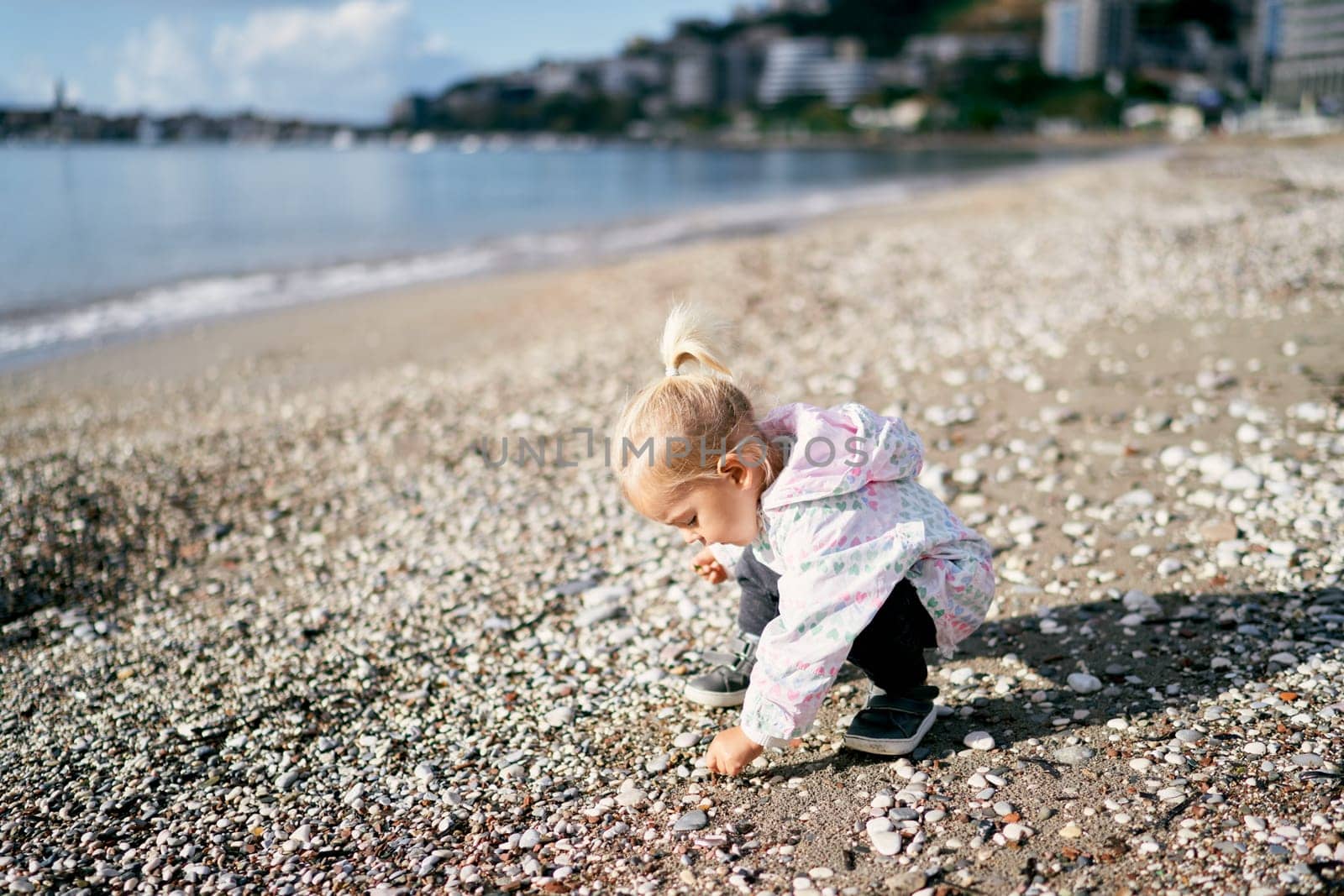 Little girl squatting on the pebbles on the beach. High quality photo