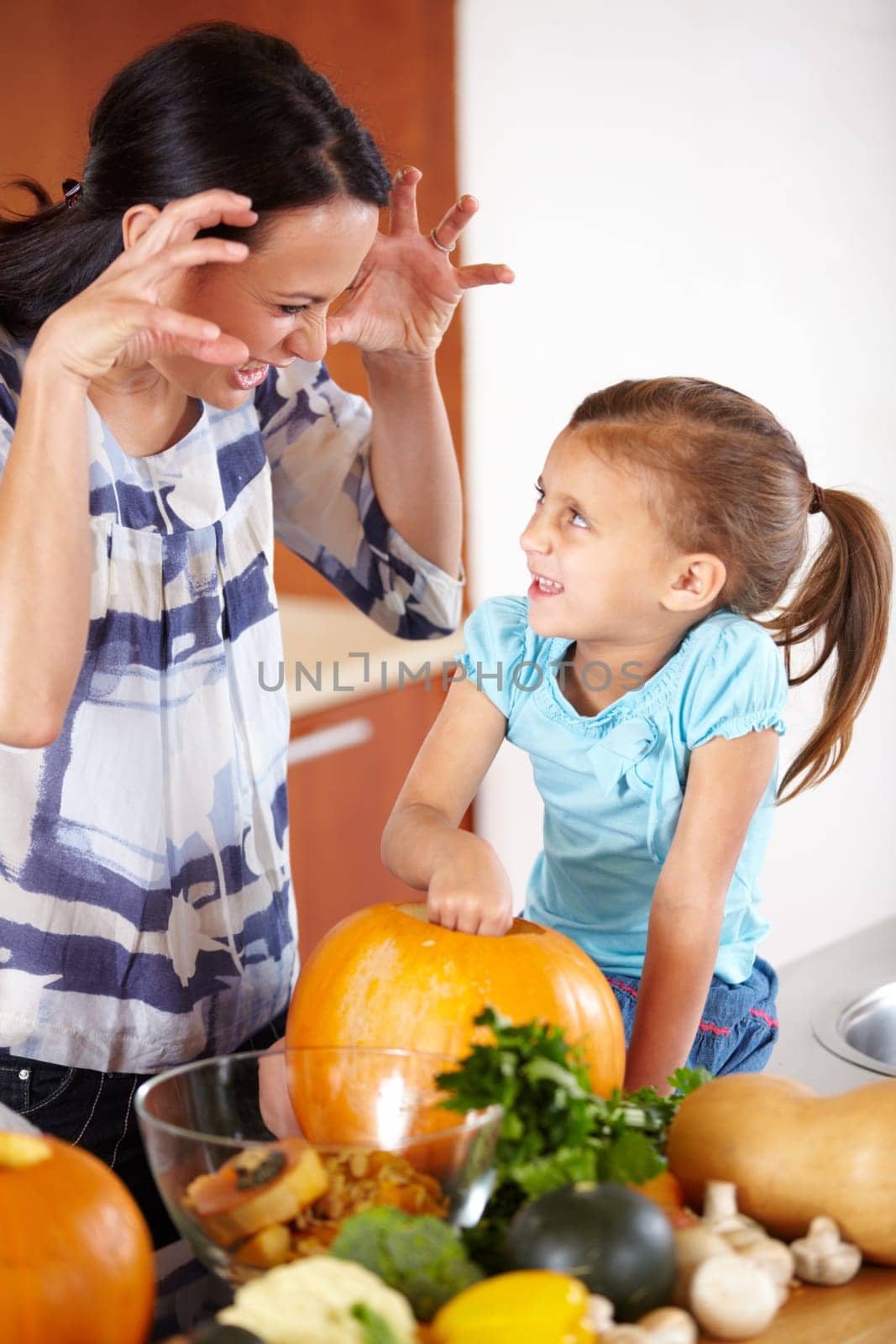 Playful, pumpkin for halloween and a mother with her daughter in the kitchen of their home together for holiday celebration. Smile, happy or funny face with a woman and girl child carving a vegetable by YuriArcurs