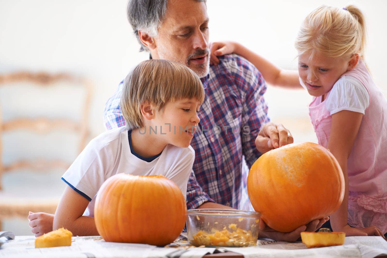 Halloween, family and carving a pumpkin with children at a home table for fun and bonding. Man or dad helping or teaching young kids with creativity, holiday lantern and craft together in a house.