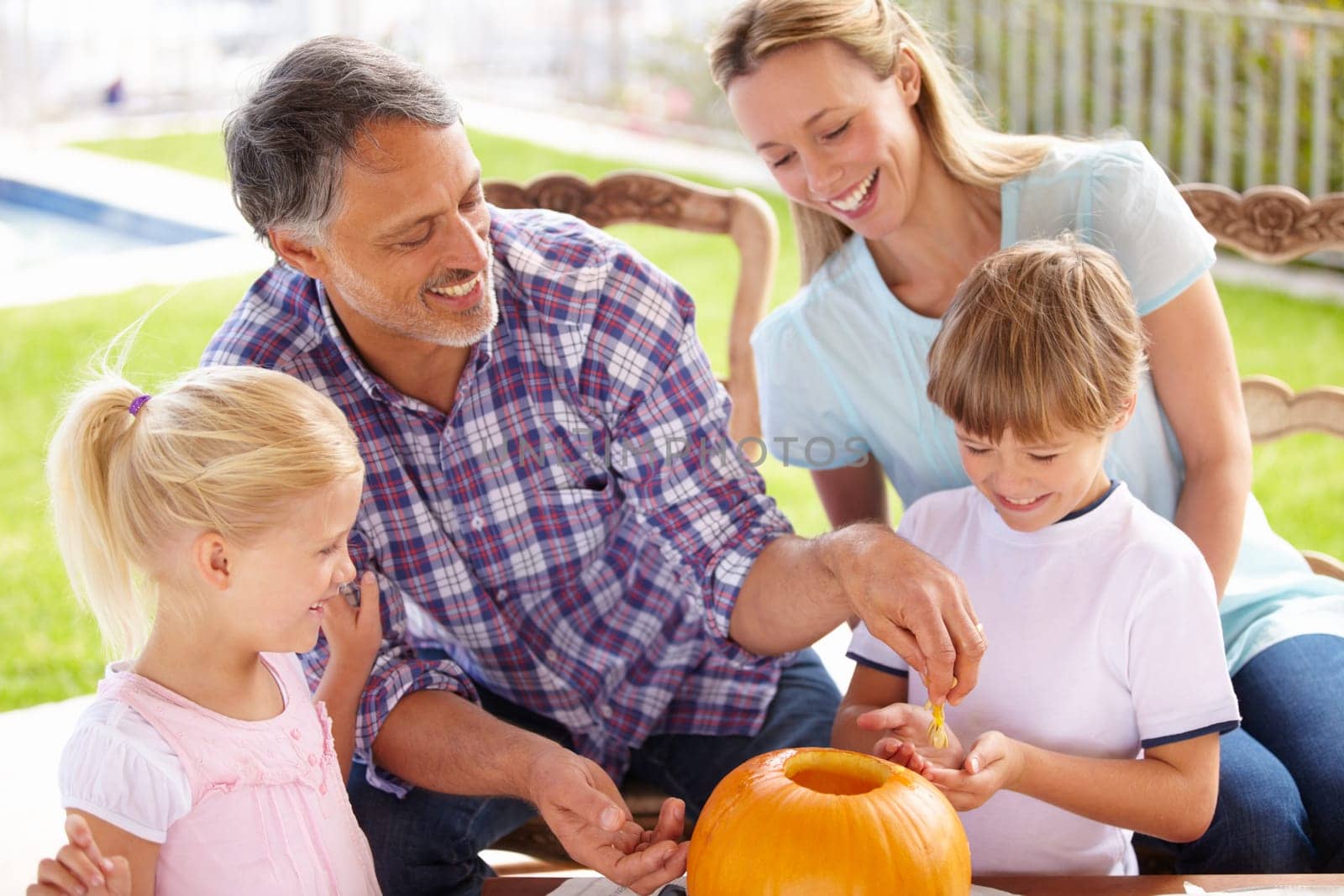 Halloween, family and carving a pumpkin with children outdoor in home backyard for fun and bonding. Man and woman or parents and young kids together for creativity, holiday lantern and happy craft.